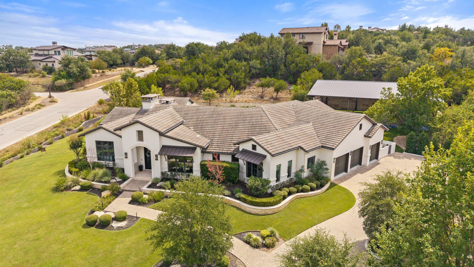 Aerial view of a white stucco home with a tiled roof, landscaped grounds, and curved driveway.
