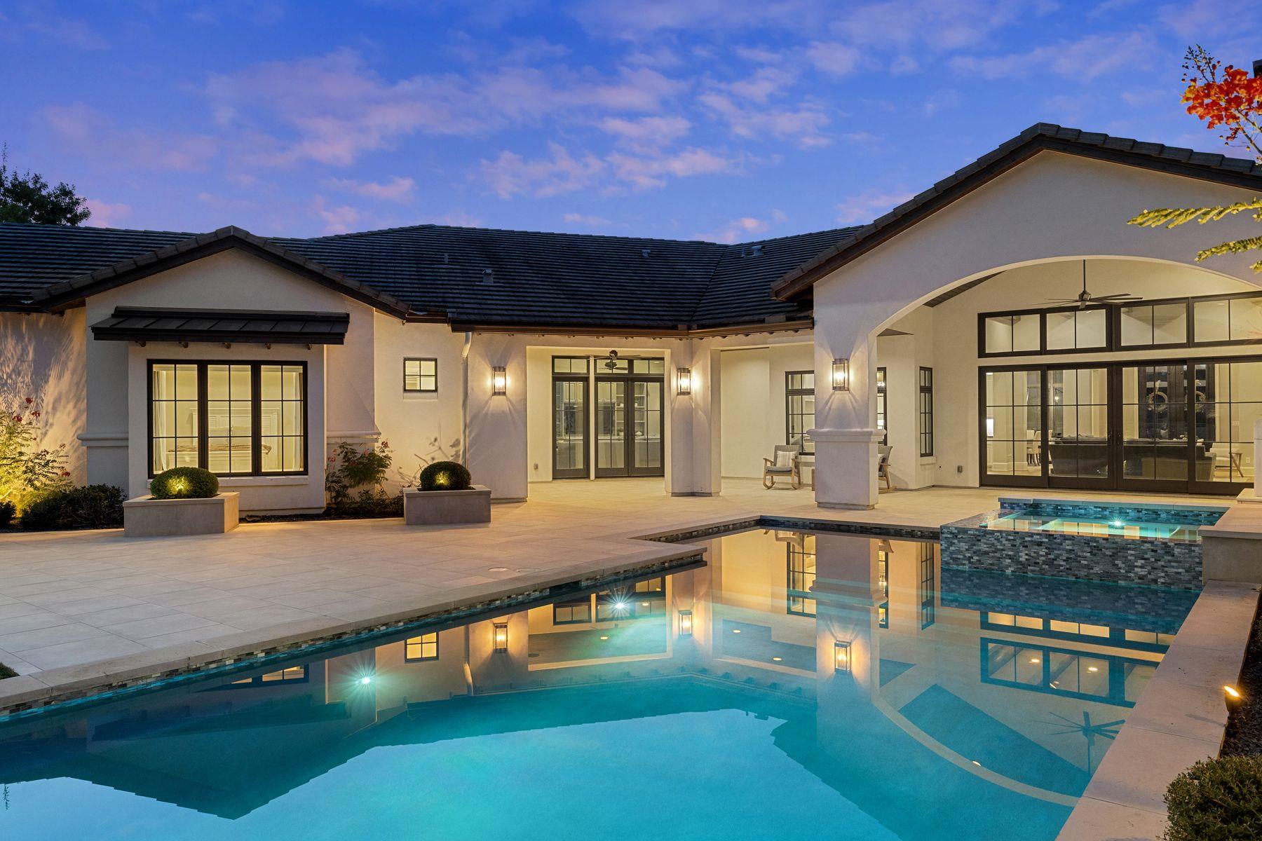 Modern home’s rear patio and illuminated pool at dusk, with the house reflected in the water.