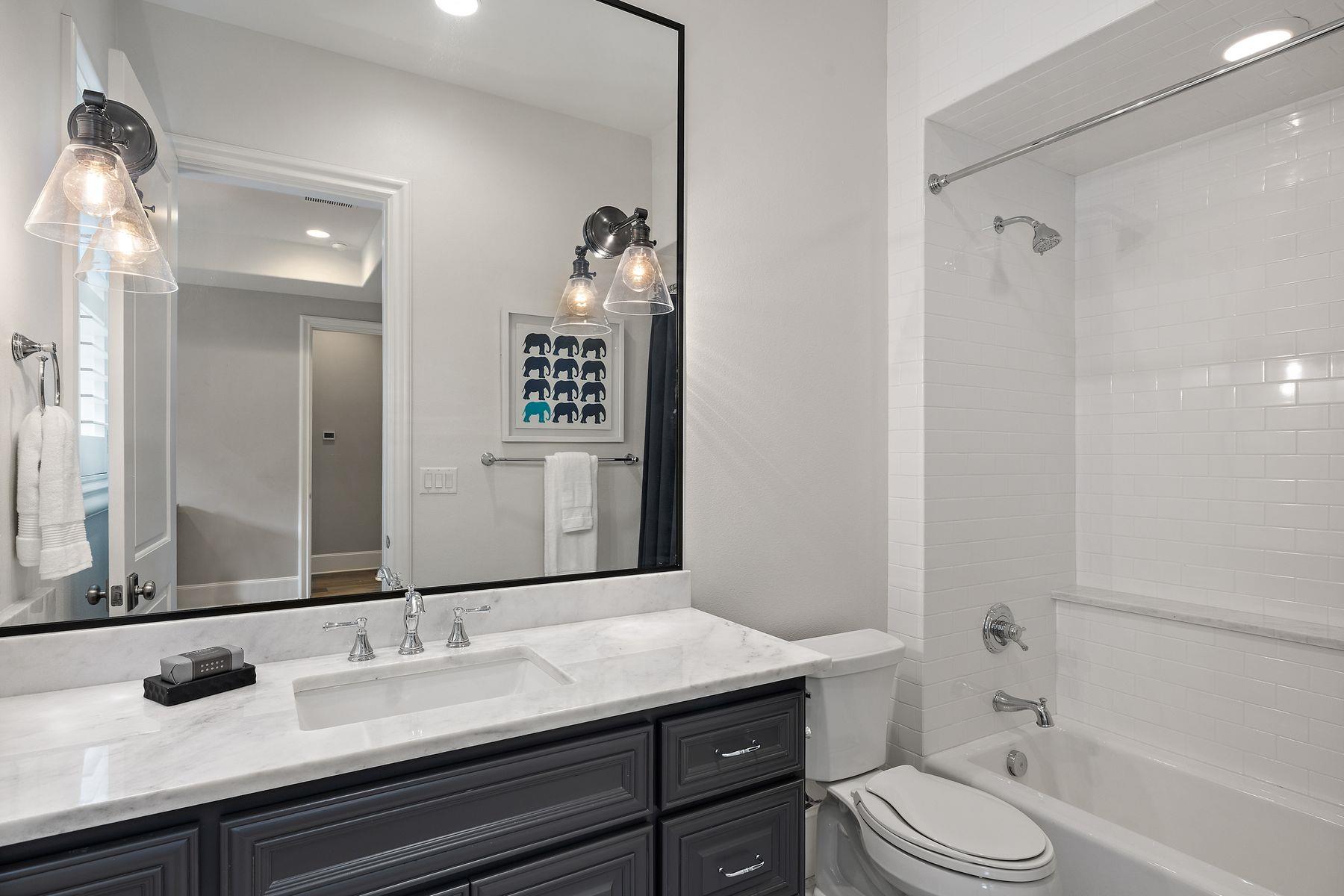 Bathroom with a dark gray vanity and marble counter beside a white subway-tile tub and shower.