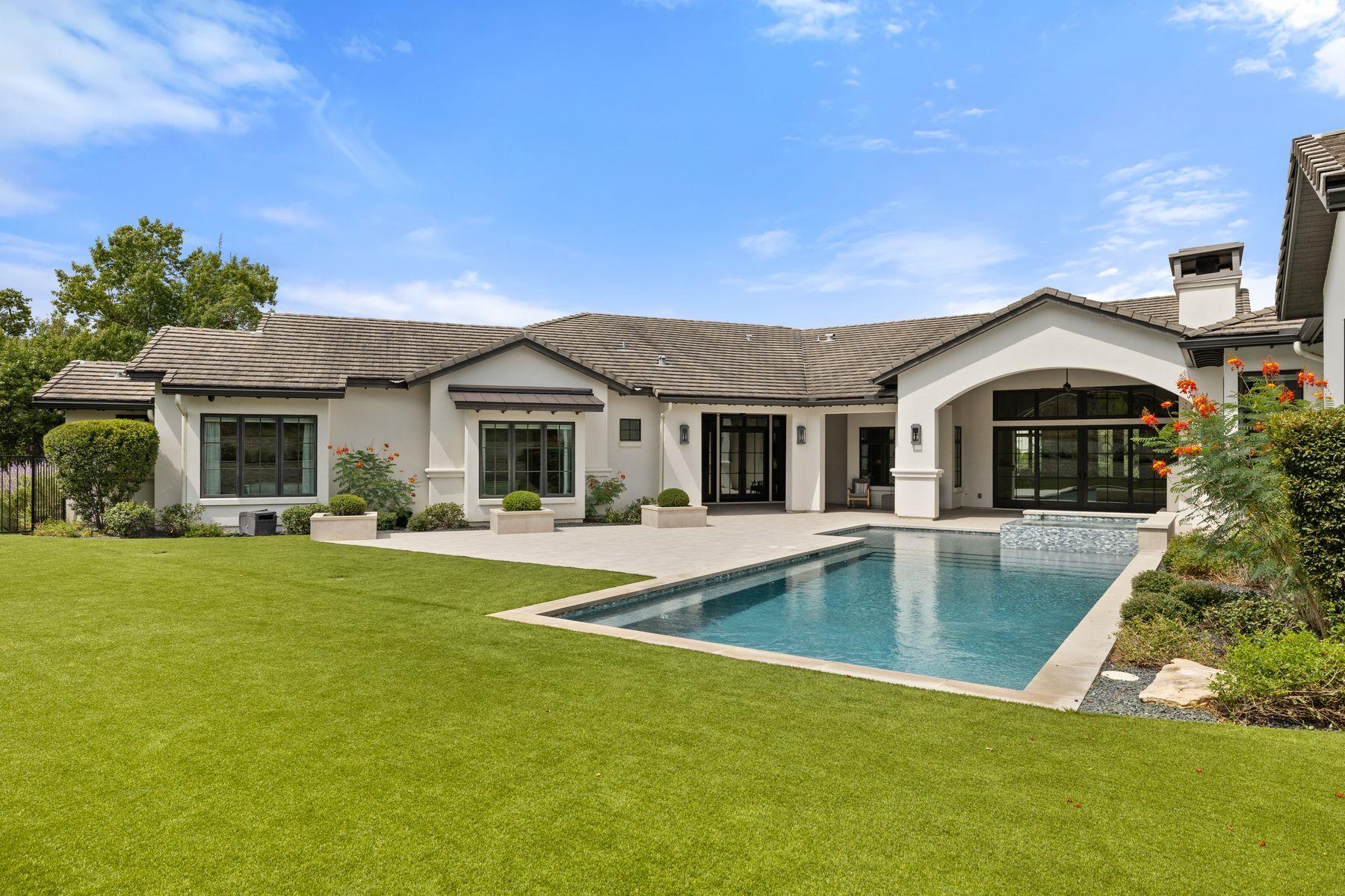 Single-story stucco home with a swimming pool, arched patio, and expansive green lawn.