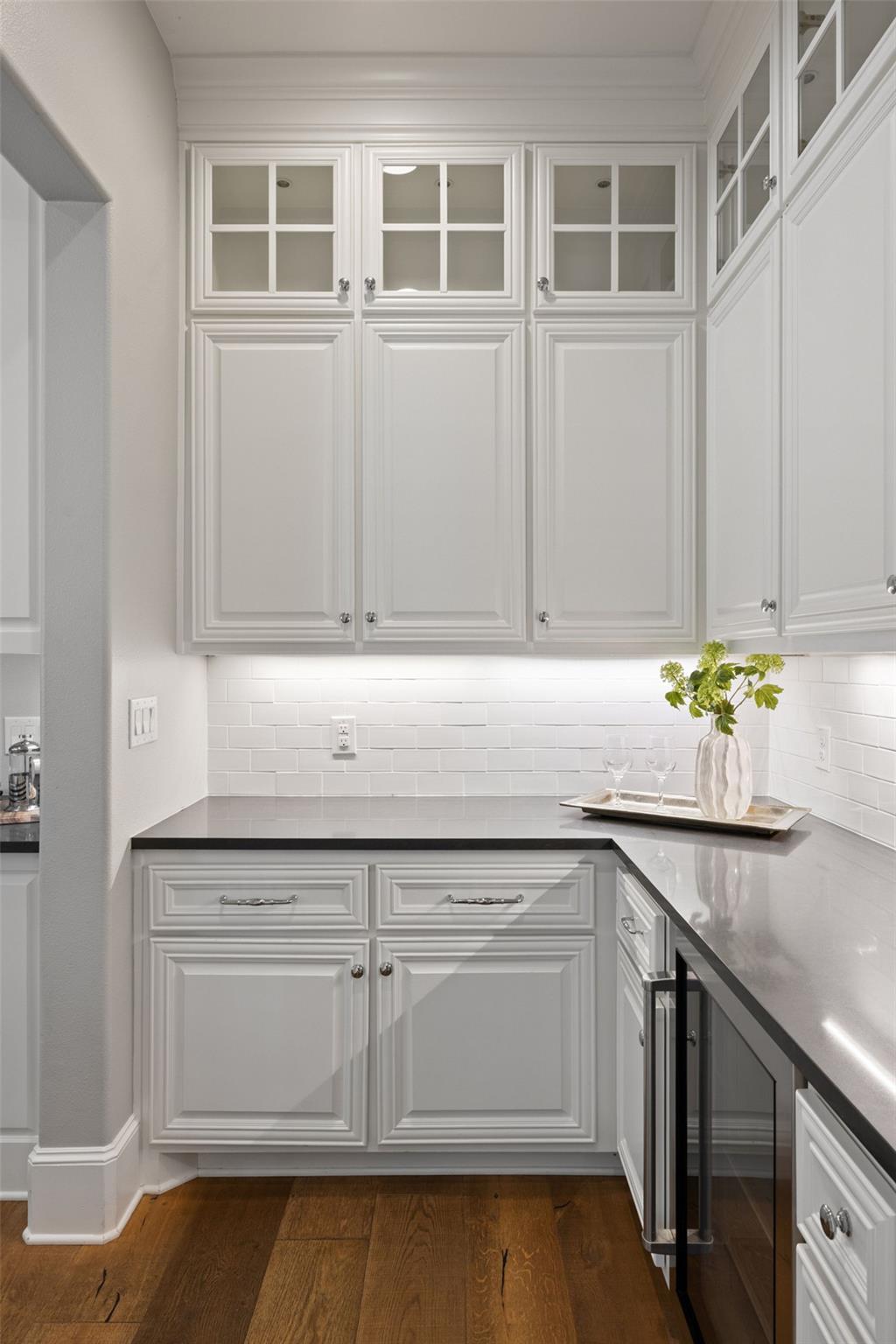 Kitchen with white raised-panel cabinetry, glass-front upper cabinets, gray counters, and a subway-tile backsplash.