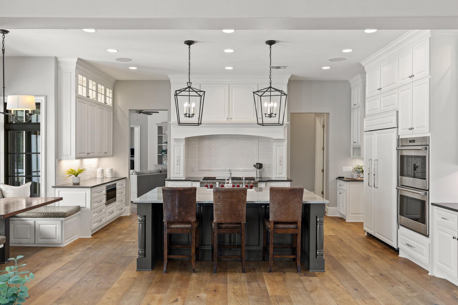 Bright kitchen with white cabinetry, dark island, leather bar stools, and two black pendant lights.