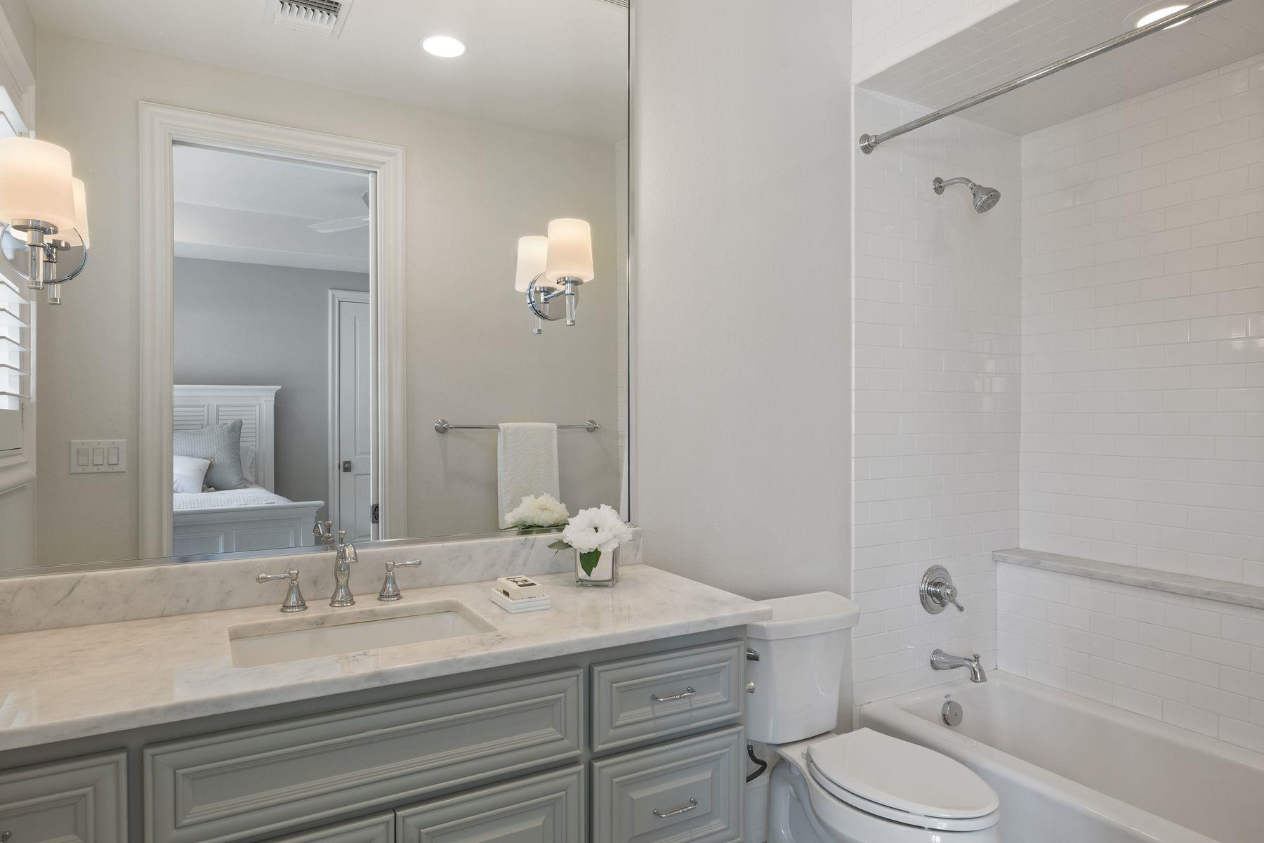 Bathroom with a gray paneled vanity, marble counter, and white subway-tile tub and shower.