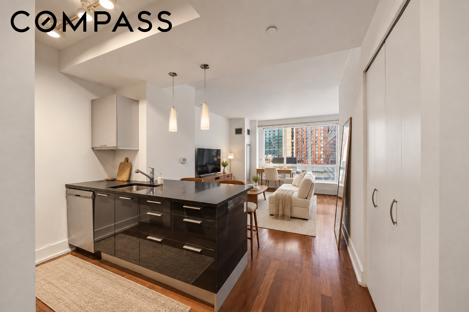 Open-plan apartment kitchen and living room with a dark island and large city-facing windows.