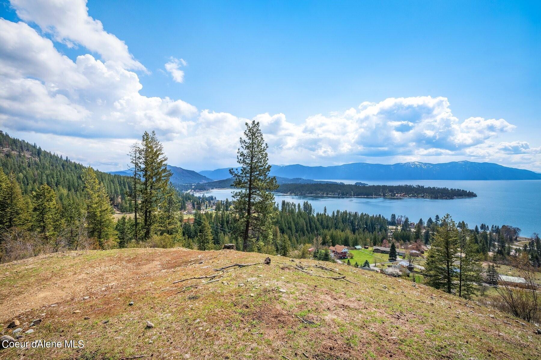 Rocky hillside lot overlooks a blue lake, wooded peninsula, and distant mountain ridges.