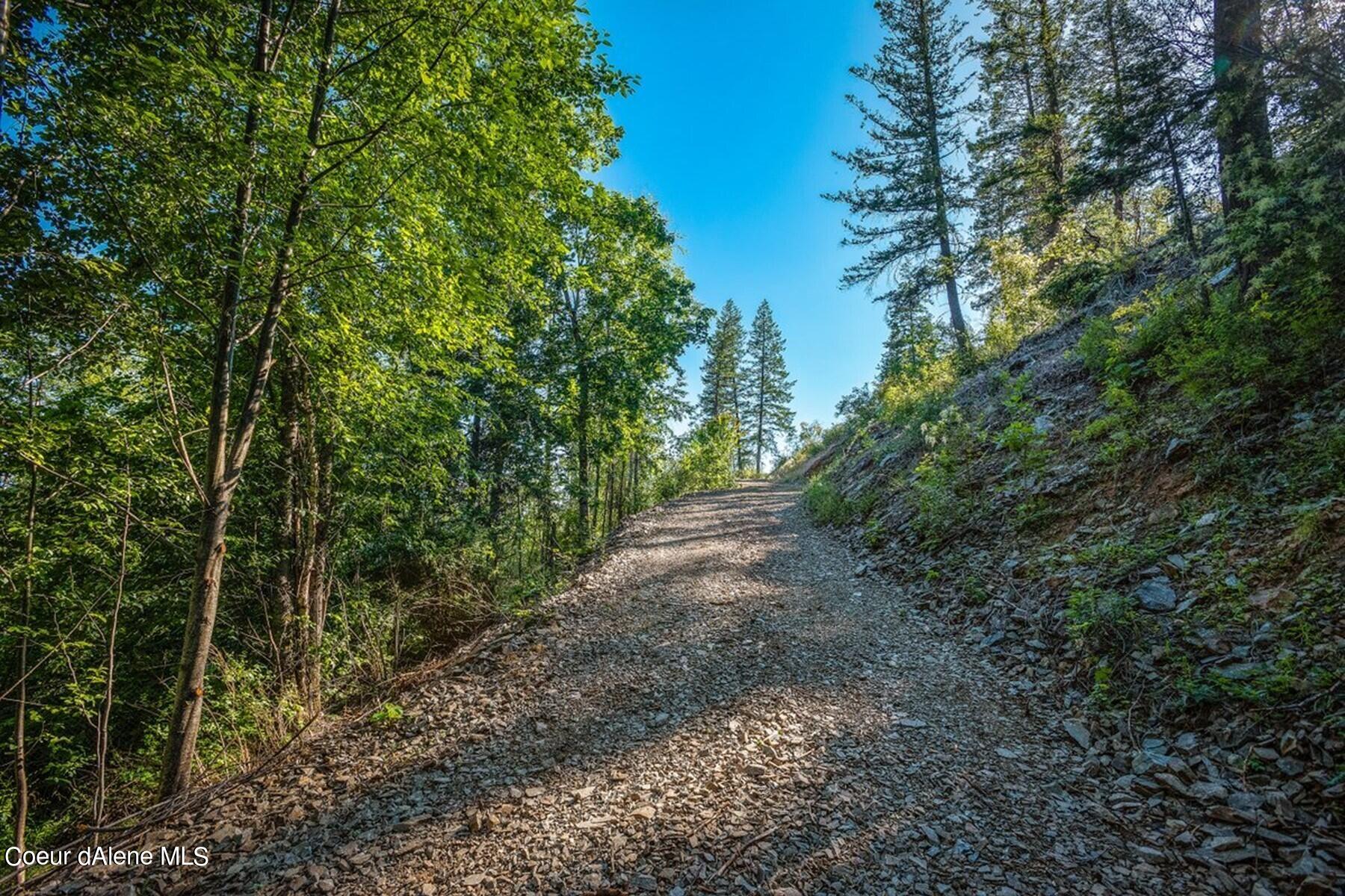 Gravel access road climbing through wooded, rocky terrain.