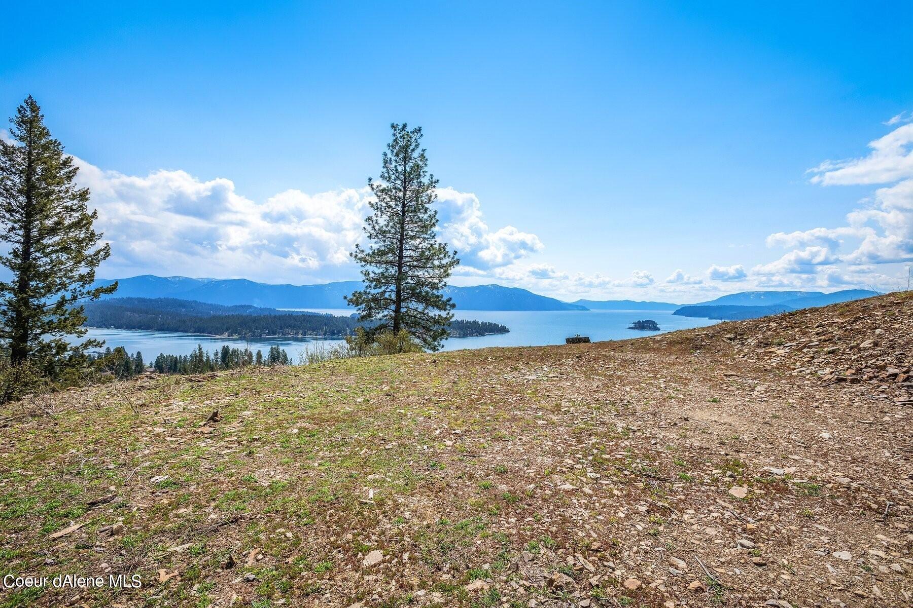 Rocky vacant hillside overlooking a lake, forested islands, and distant mountains.