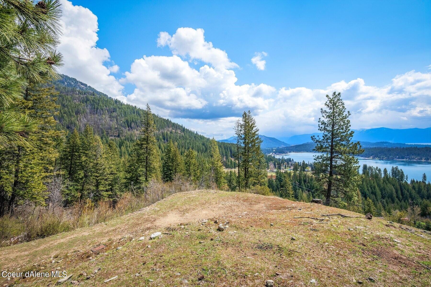 Cleared hillside lot overlooking a lake and distant mountain ridges, framed by evergreen trees.