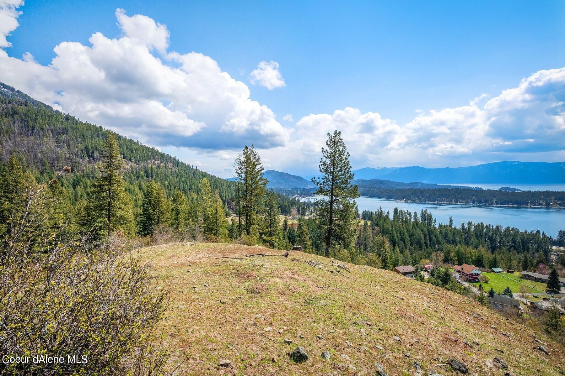 Hillside lot overlooking Lake Coeur d'Alene, with forested mountains and homes below.