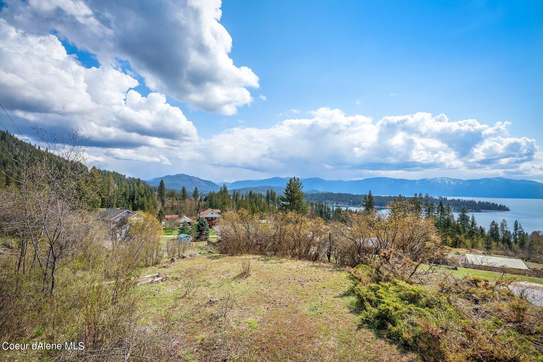 Vacant hillside lot overlooking a lake, forested shoreline, and distant mountains.