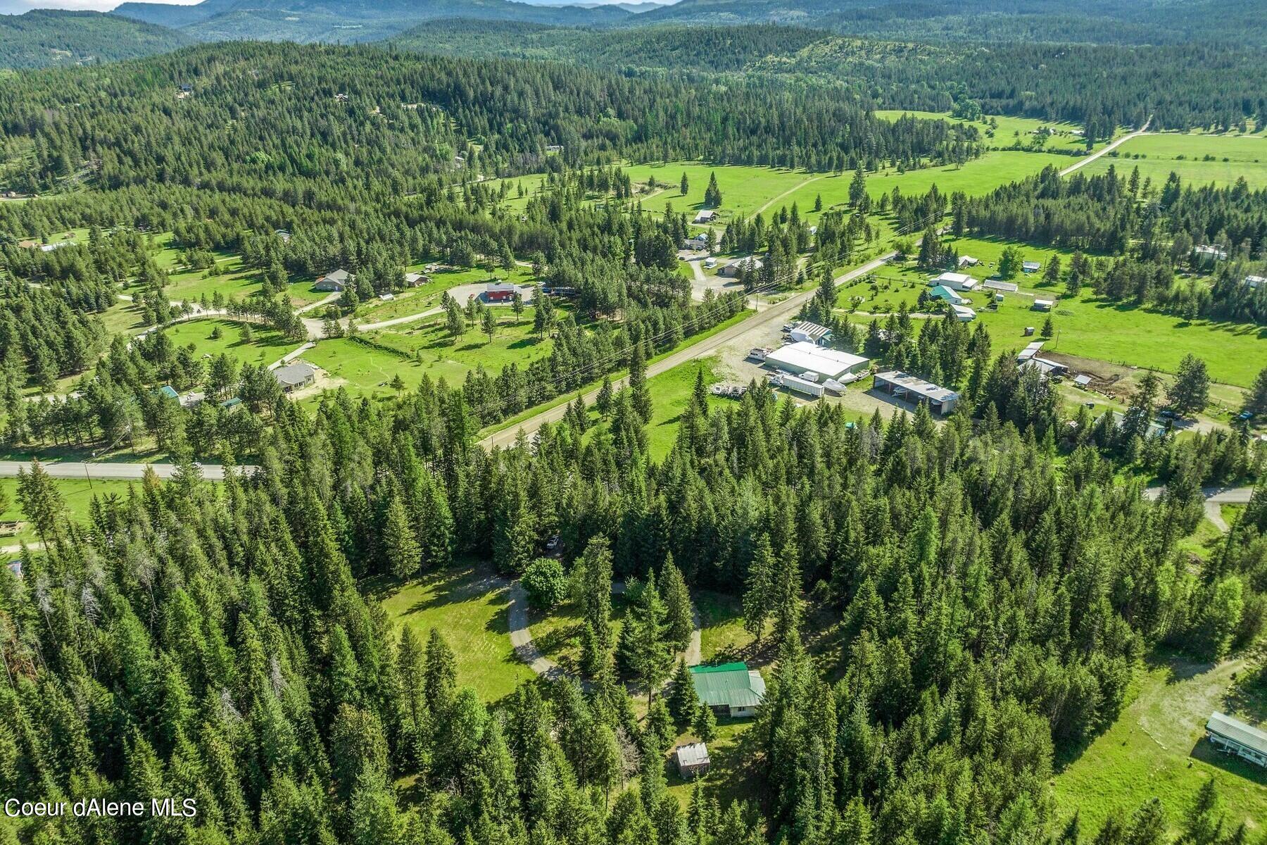 Aerial view of a rural property with open fields, scattered buildings, and forested mountains.