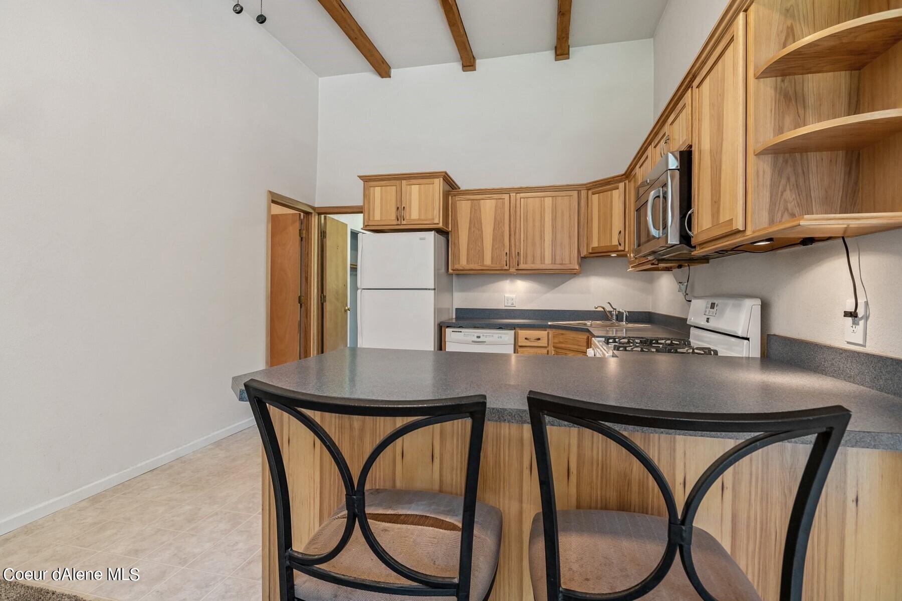 Kitchen with wood cabinets, exposed ceiling beams, and a gray peninsula with two chairs.