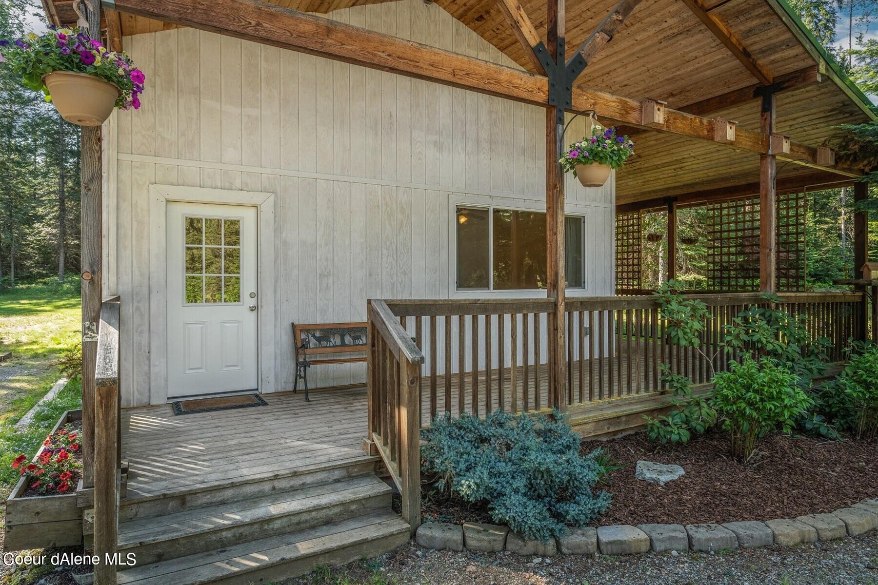 Home’s covered front porch with timber beams, wooden railings, hanging flowers, and landscaped beds.