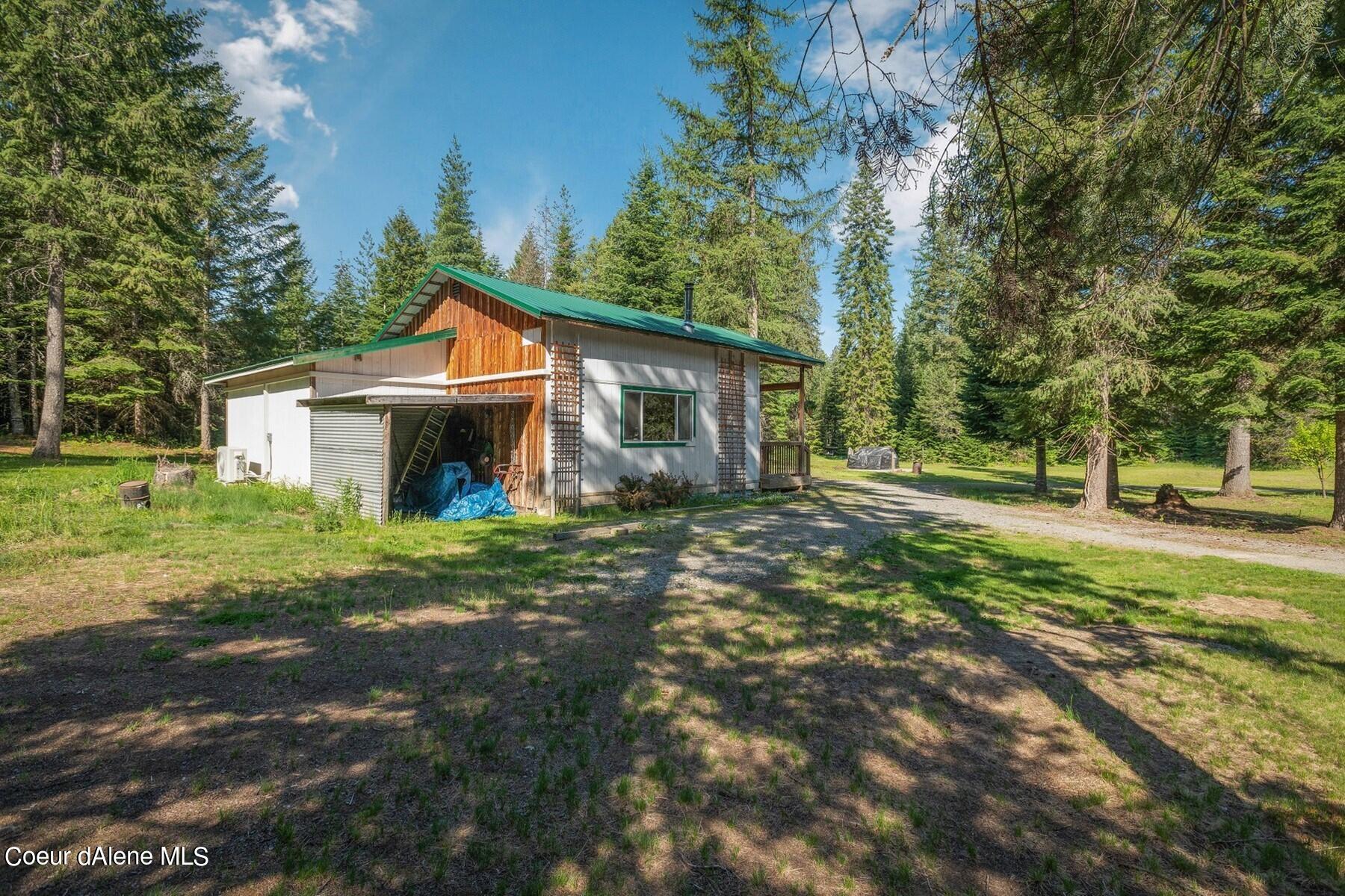 Cabin-style home with a green metal roof and open garage bay in a wooded clearing.