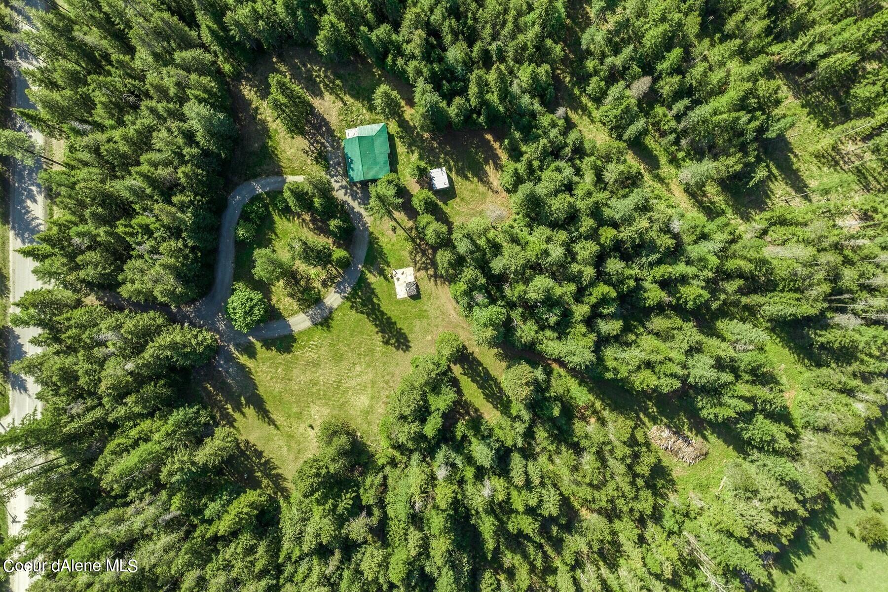 Aerial view of a wooded property with a green-roofed building and winding driveway.