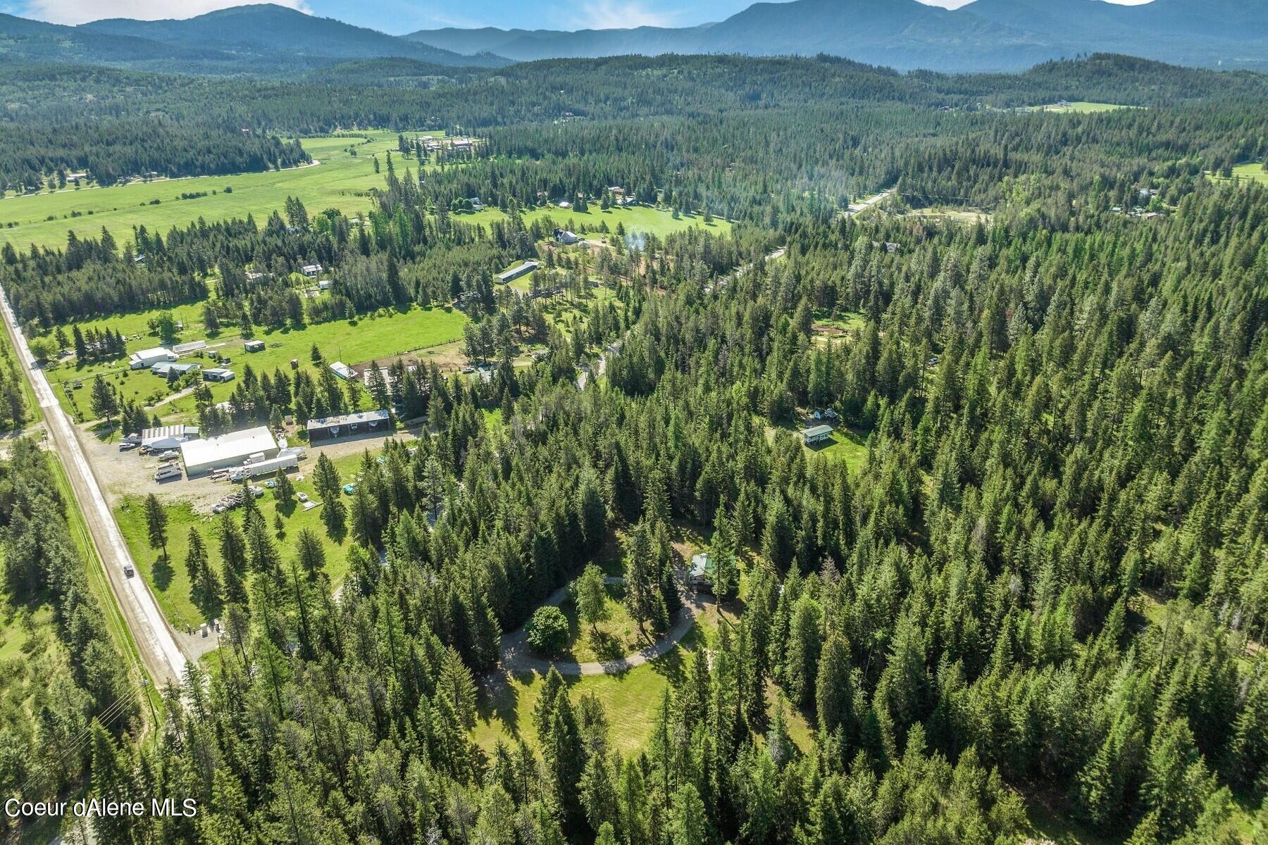 Aerial view of wooded acreage with open fields, outbuildings, and distant mountains.