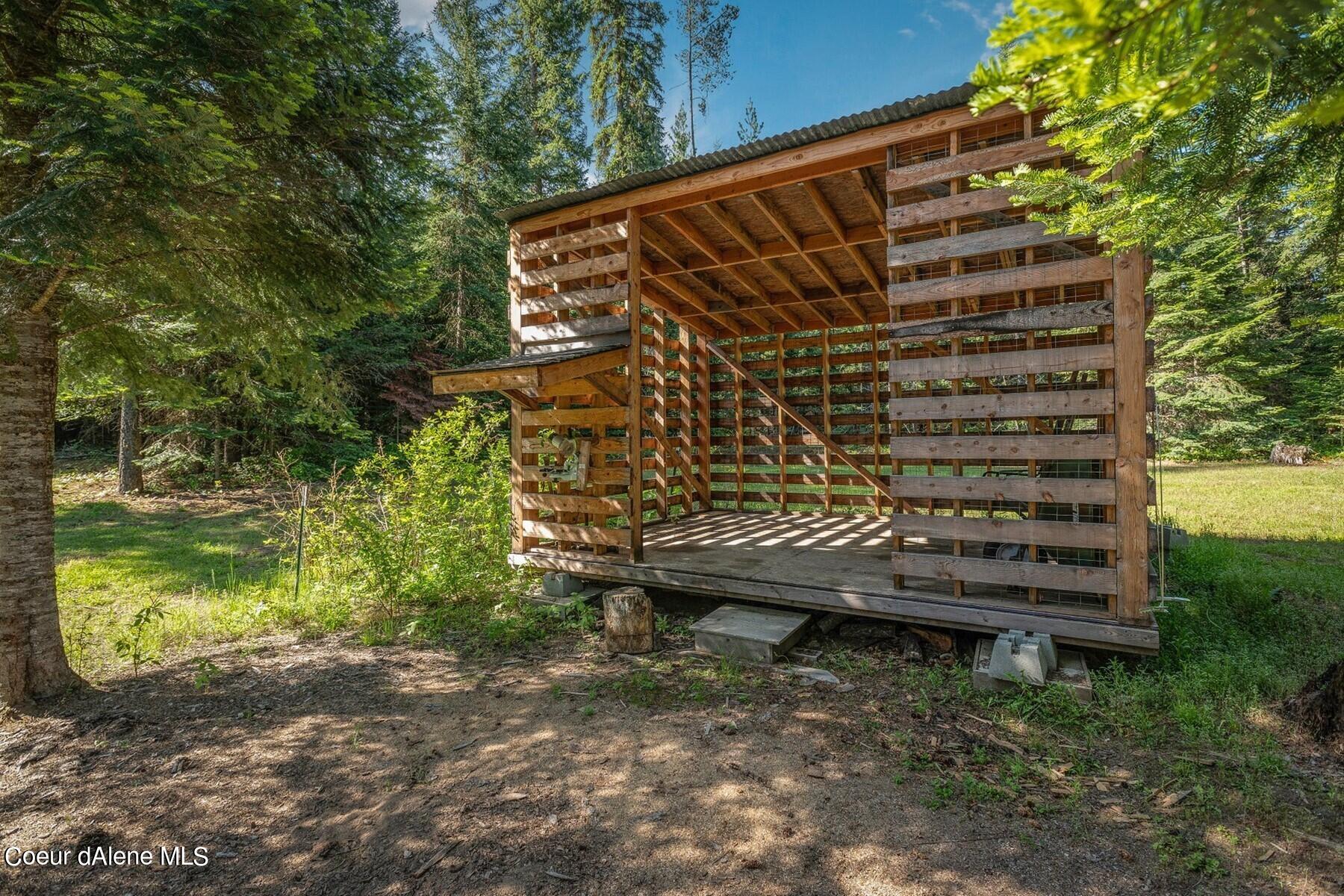 Open-sided timber shelter with exposed roof framing in a wooded clearing.