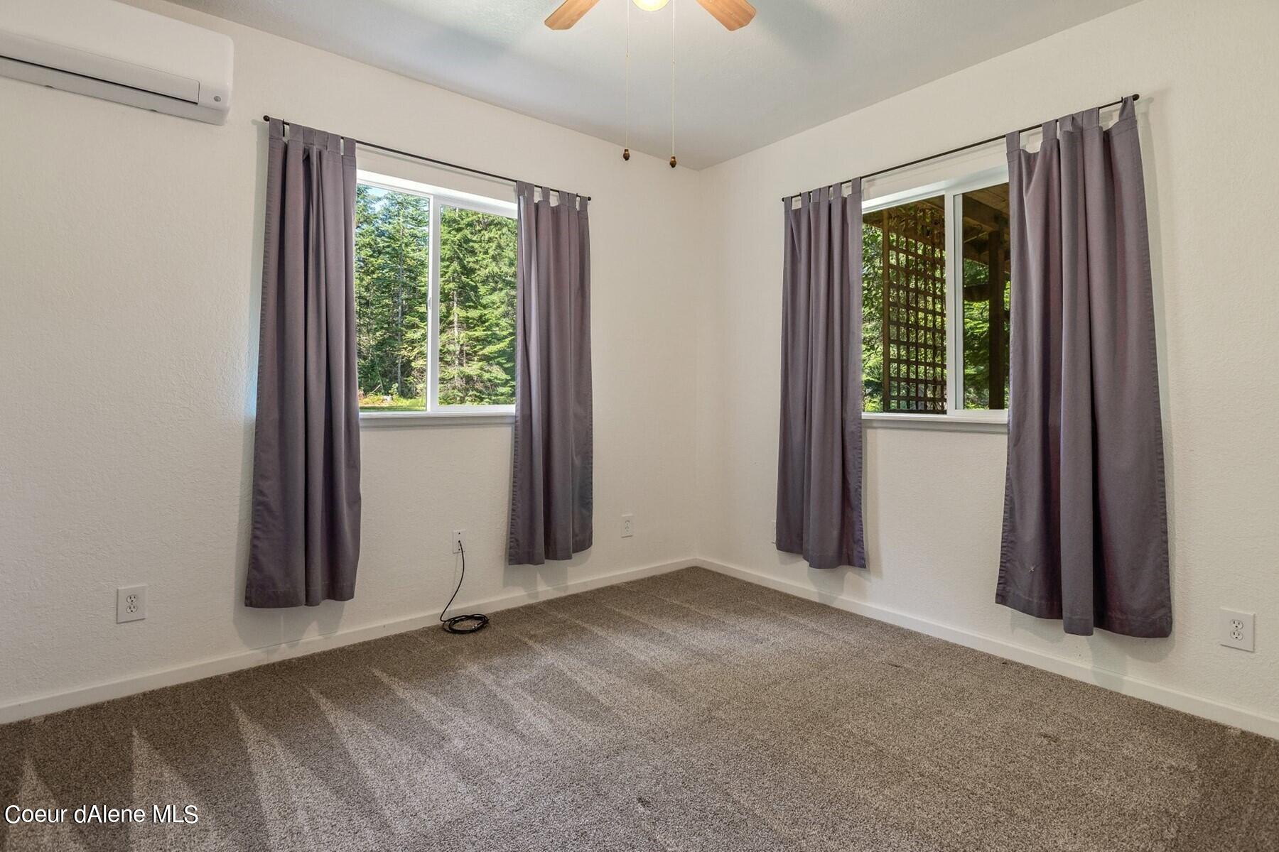 Empty carpeted bedroom with gray curtains, two windows, and a wall-mounted air conditioner.