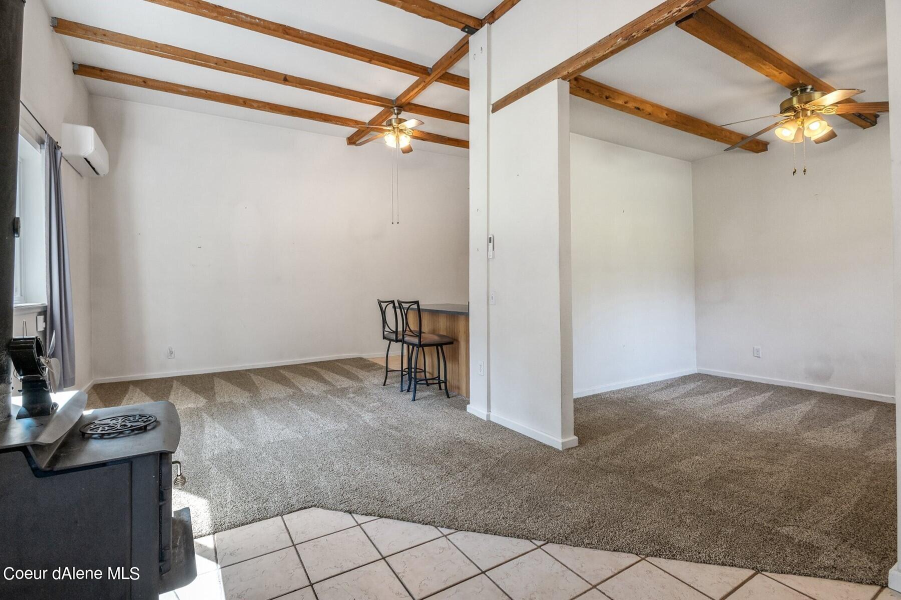 Open living room with exposed wood ceiling beams, carpet, and a counter with bar stools.