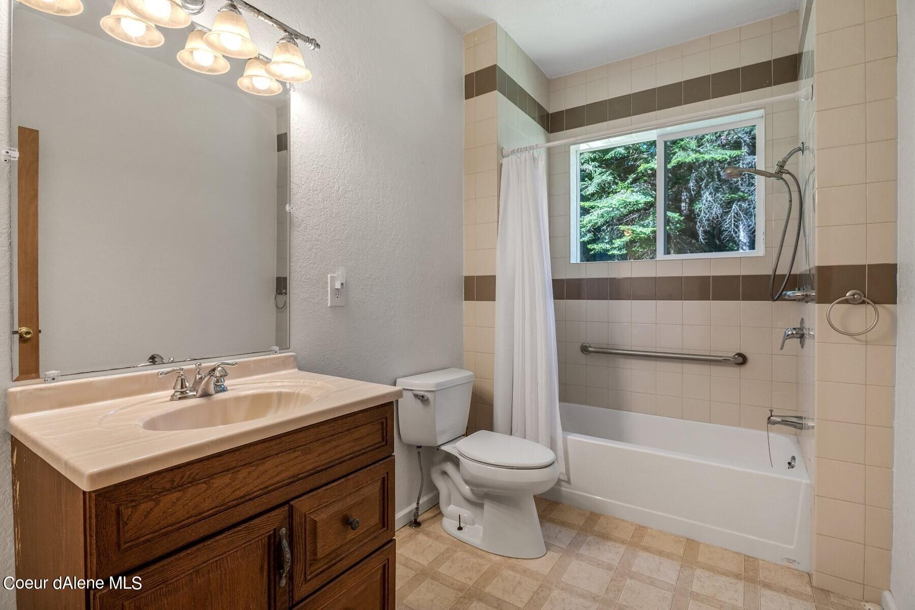 Bathroom with a dark wood vanity and tiled tub-shower beneath a window overlooking trees.
