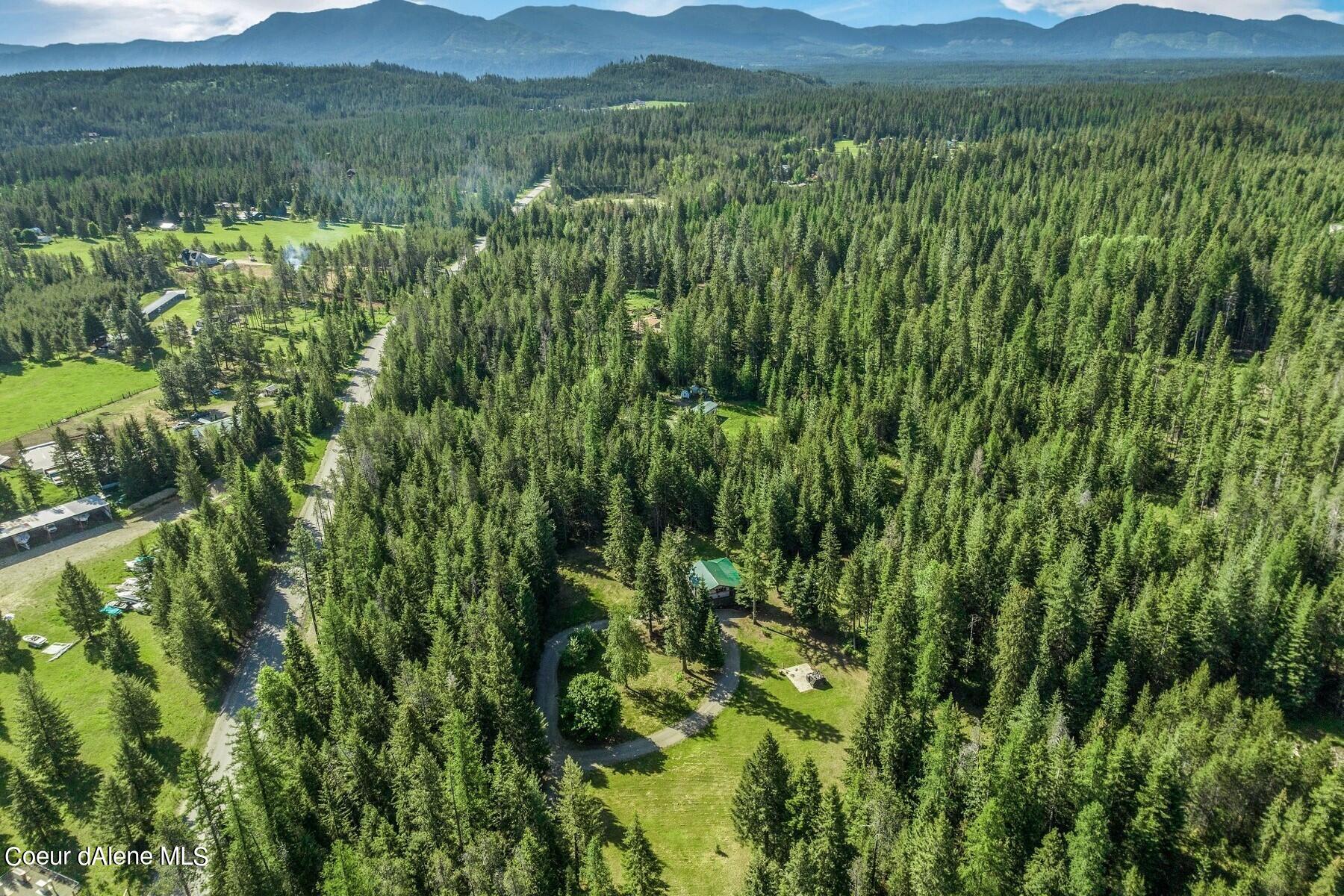 Aerial view of a wooded property with grassy clearings, scattered buildings, and mountains in the distance.