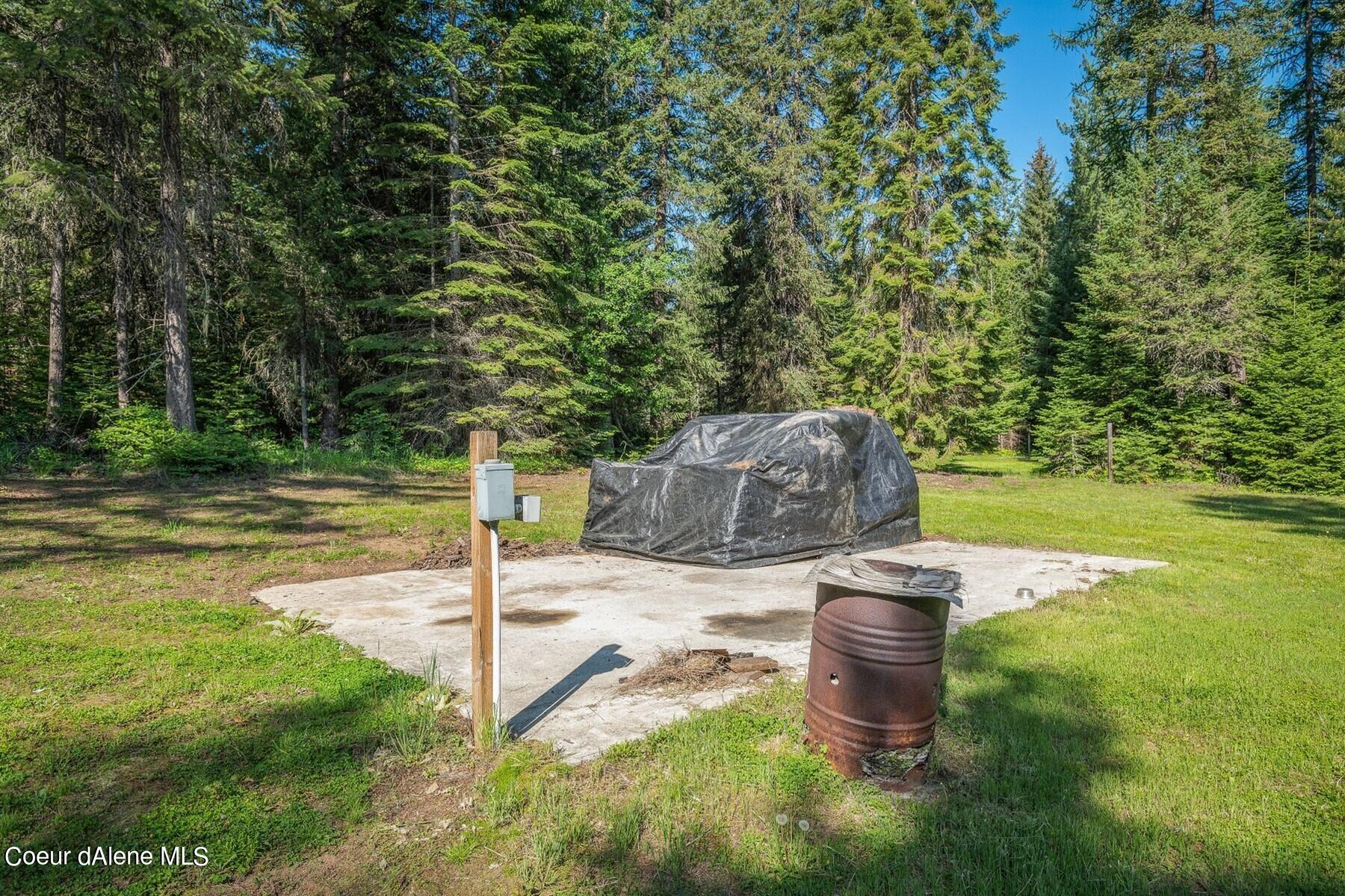 Wooded property clearing with a concrete pad and tarp-covered equipment.