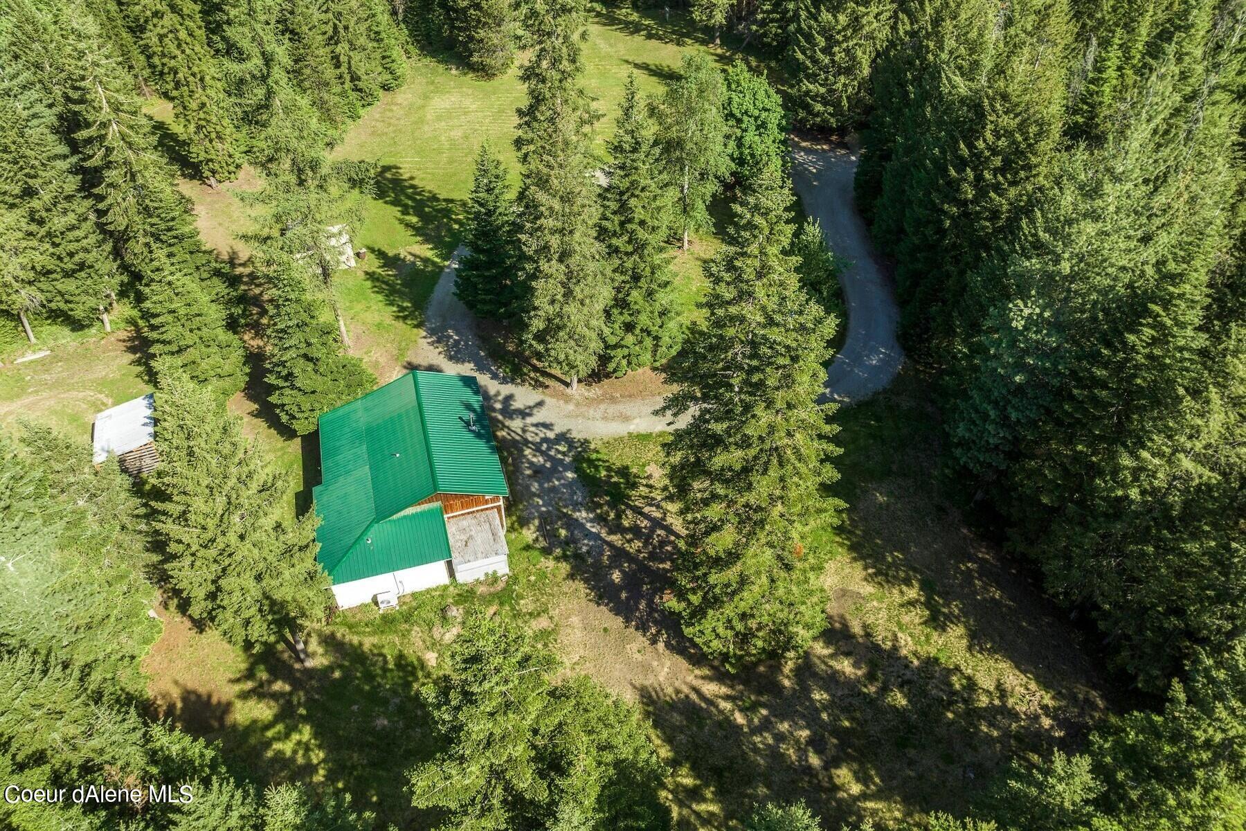 Aerial view of a green-roofed building and gravel drive amid a wooded property.