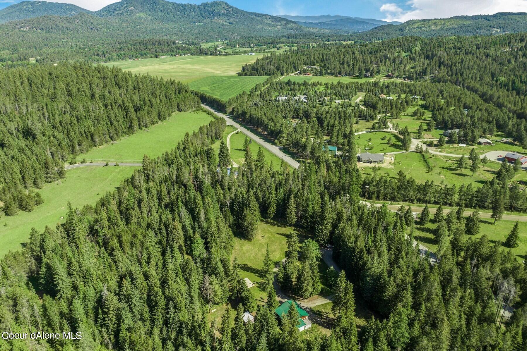 Aerial view of a wooded rural property with open meadows, winding roads, and forested mountains.