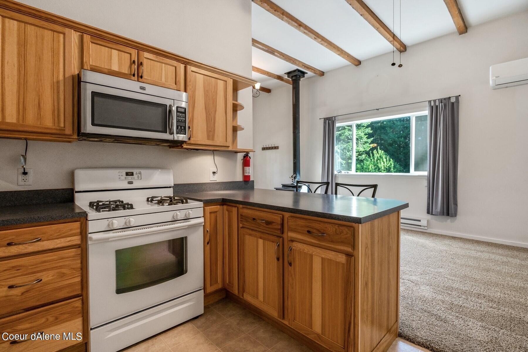 Kitchen with wood cabinets, a dark peninsula, exposed ceiling beams, and a window overlooking greenery.