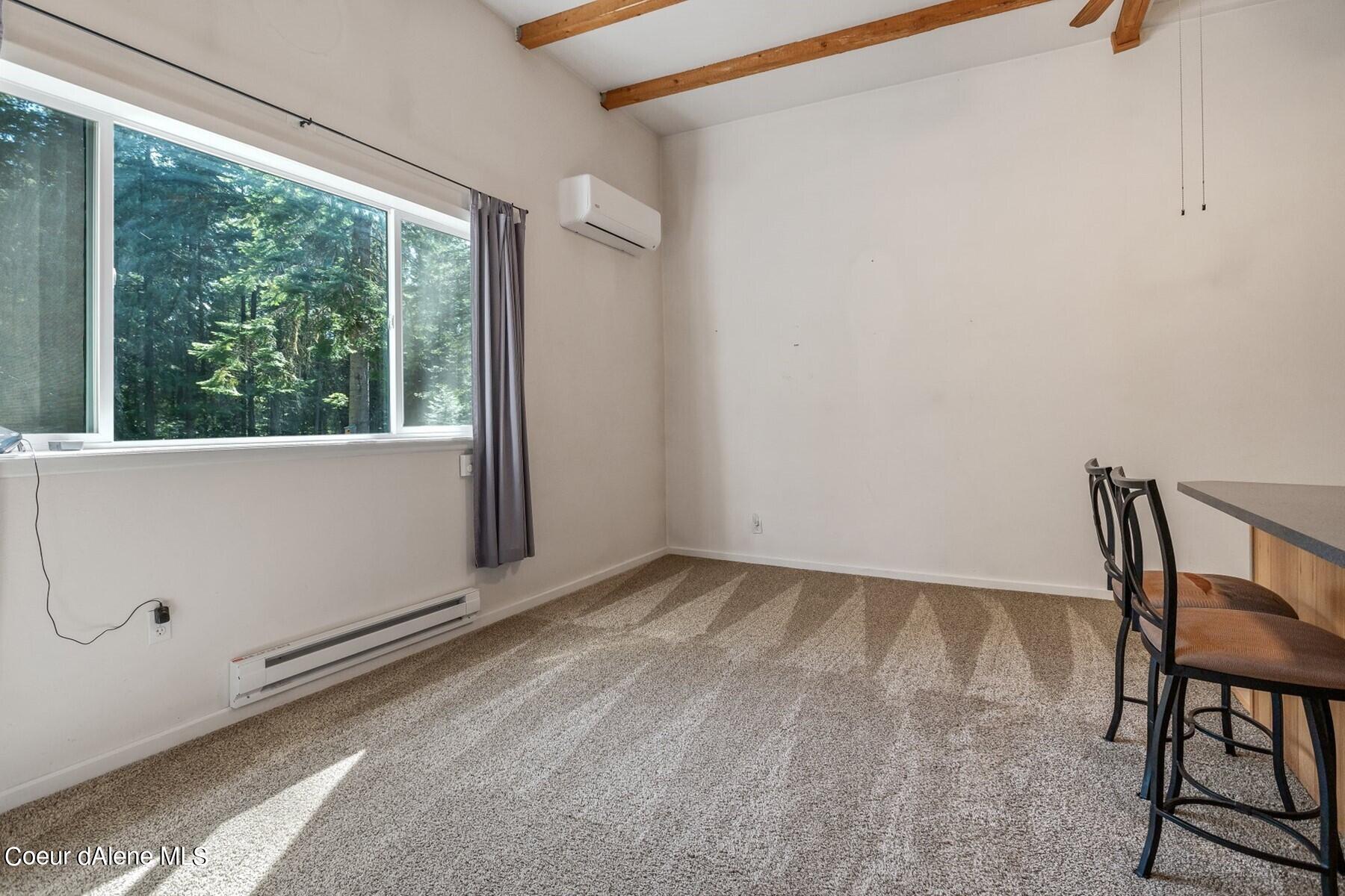 Carpeted dining area with exposed wood beams, a large forest-facing window, and two counter chairs.