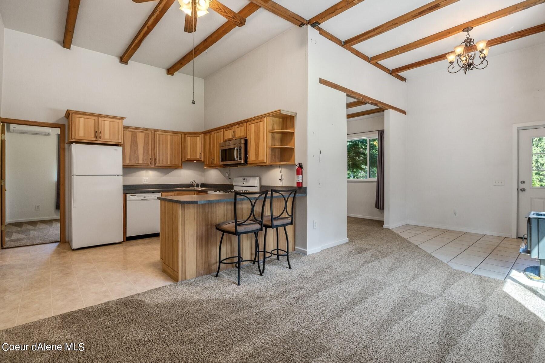 Open kitchen and living area with wood cabinetry, breakfast island, and exposed ceiling beams.