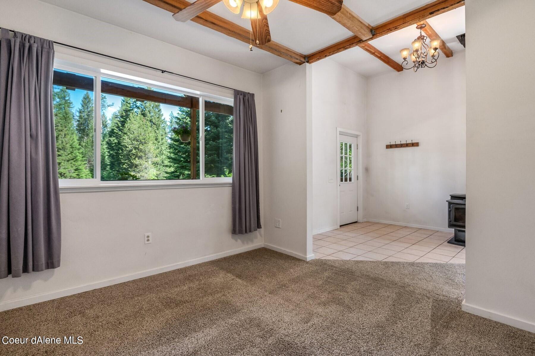 Living room with exposed wood ceiling beams, a wide forest-facing window, and carpet adjoining tile.