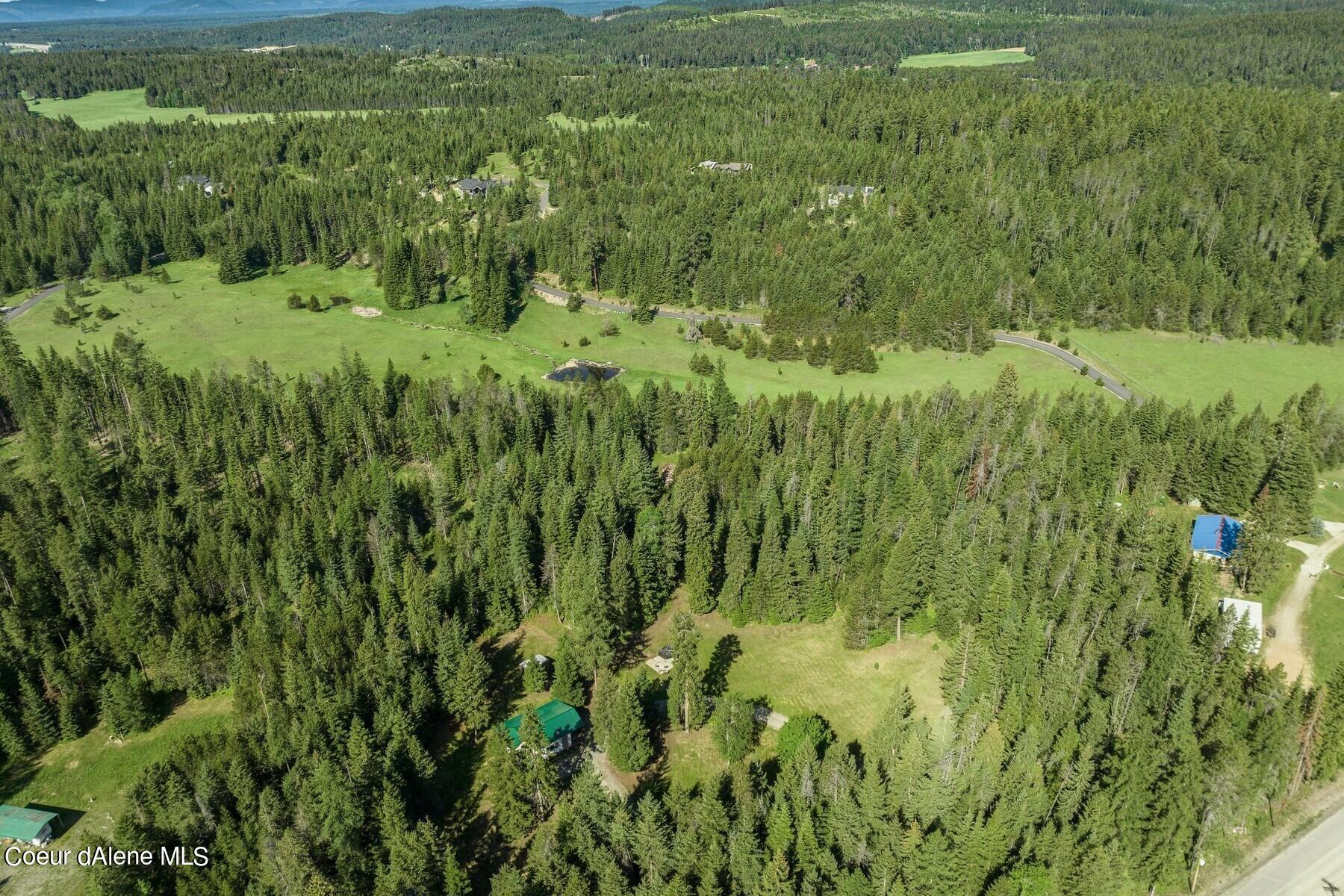 Aerial view of wooded land with open meadows, scattered homes, a winding road, and a small pond.