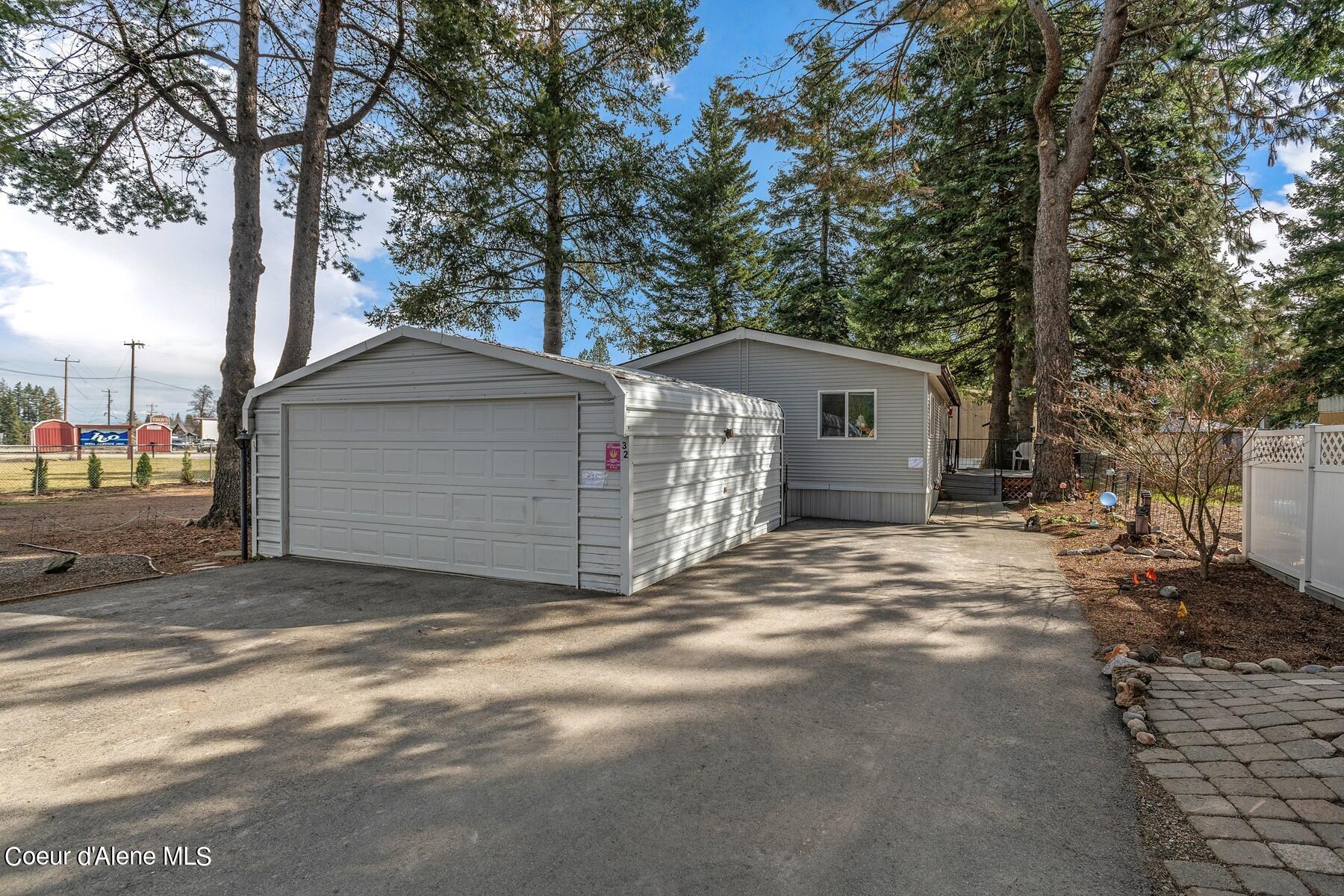 Gray home behind a detached garage, with a broad driveway and mature trees.