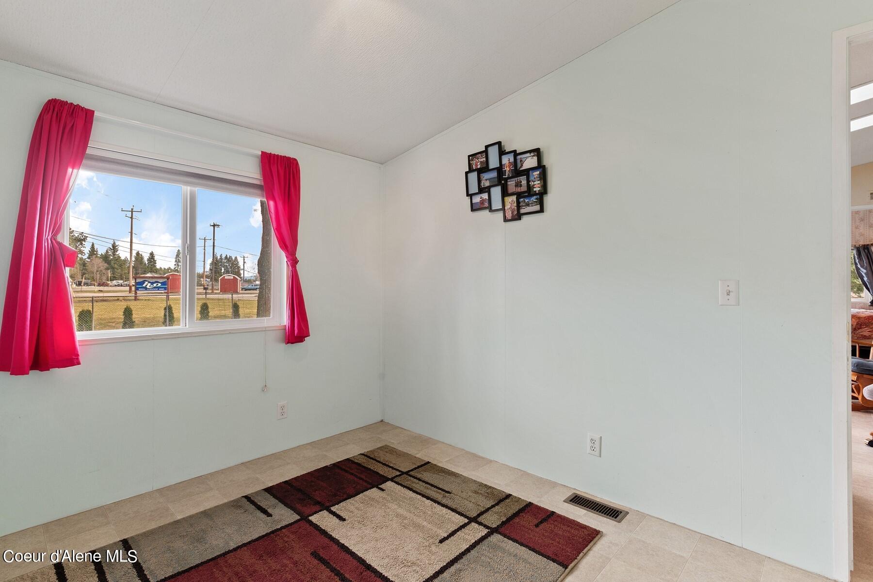 Mostly empty room with pink window curtains and a geometric rug.