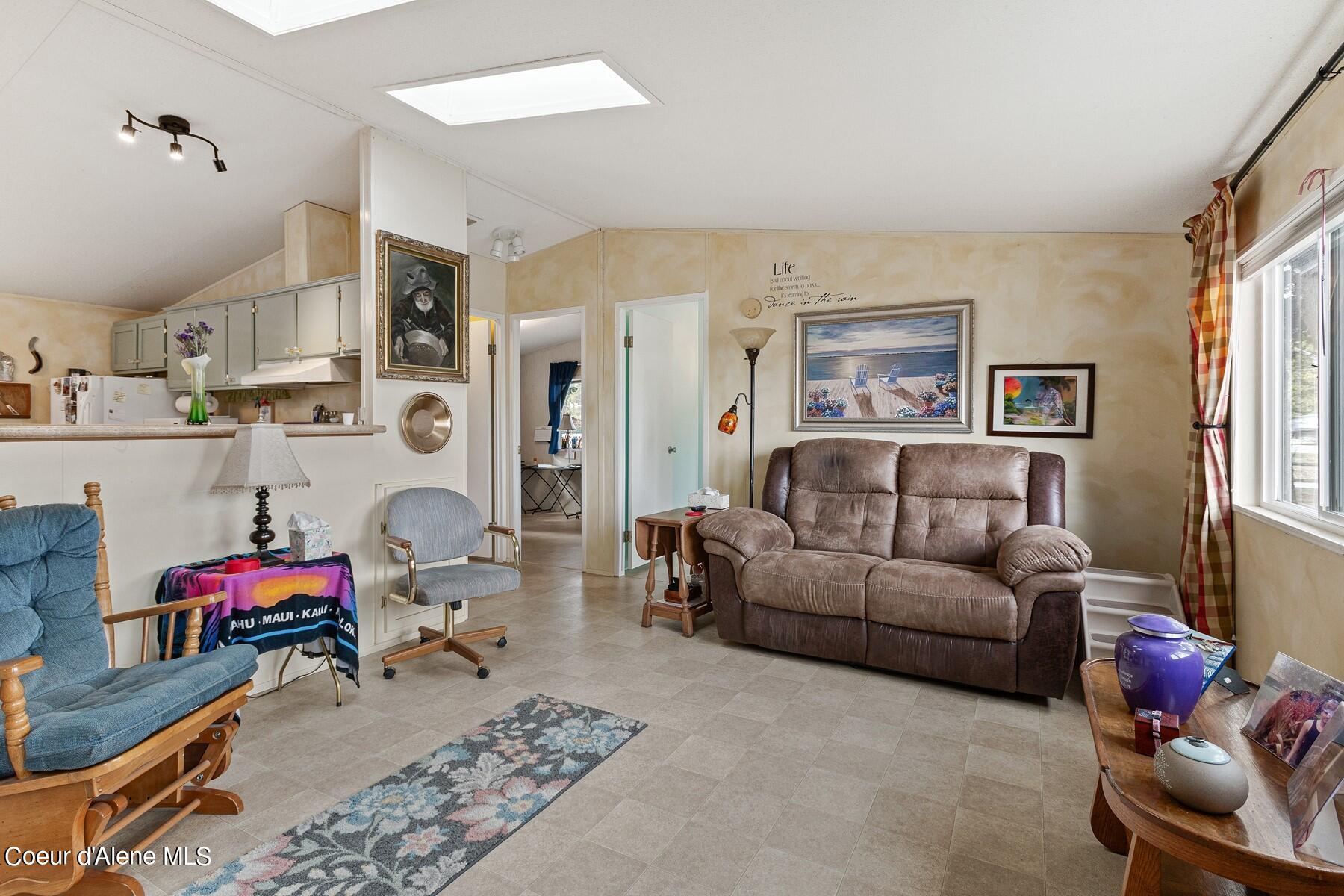 Furnished living room with brown reclining sofa, blue chairs, and an adjoining kitchen.
