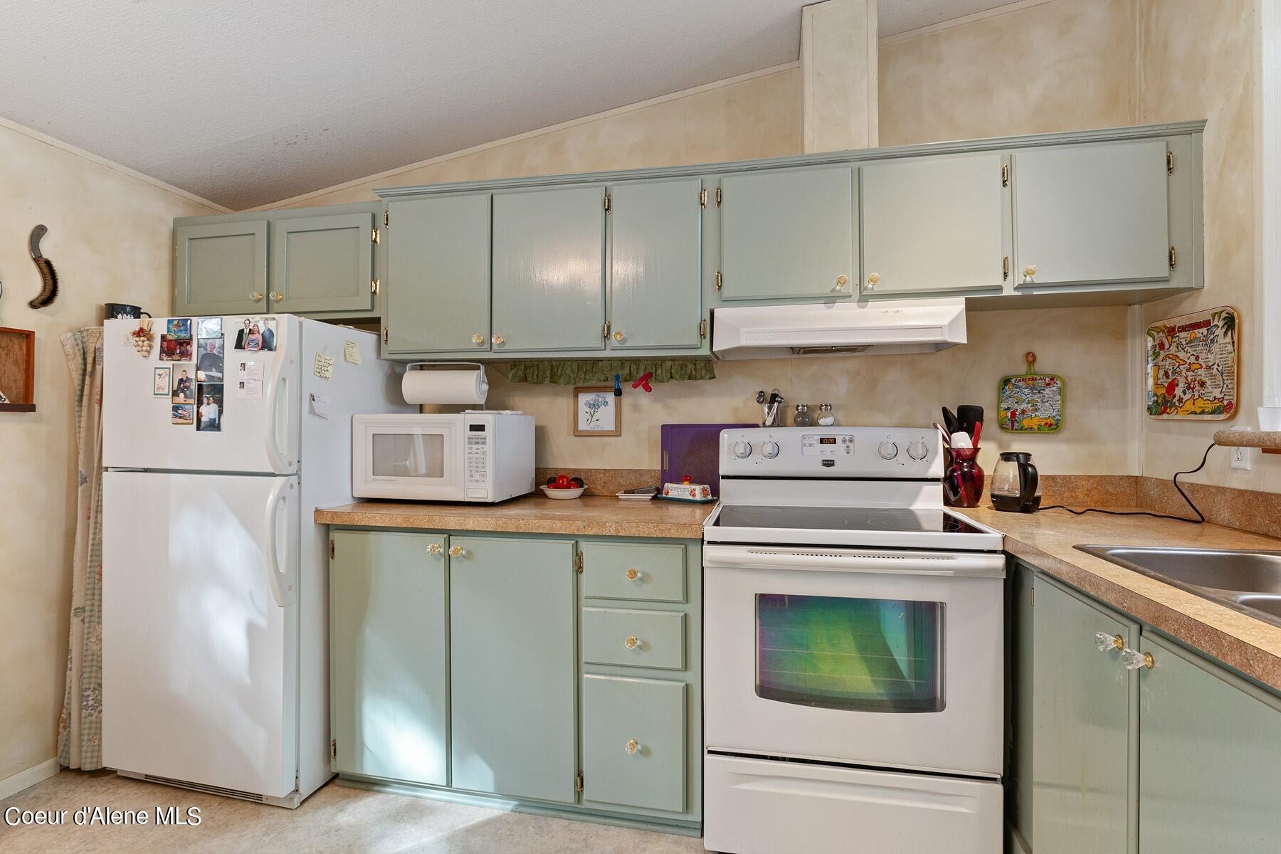 Kitchen with sage-green cabinets, white appliances, and tan countertops.