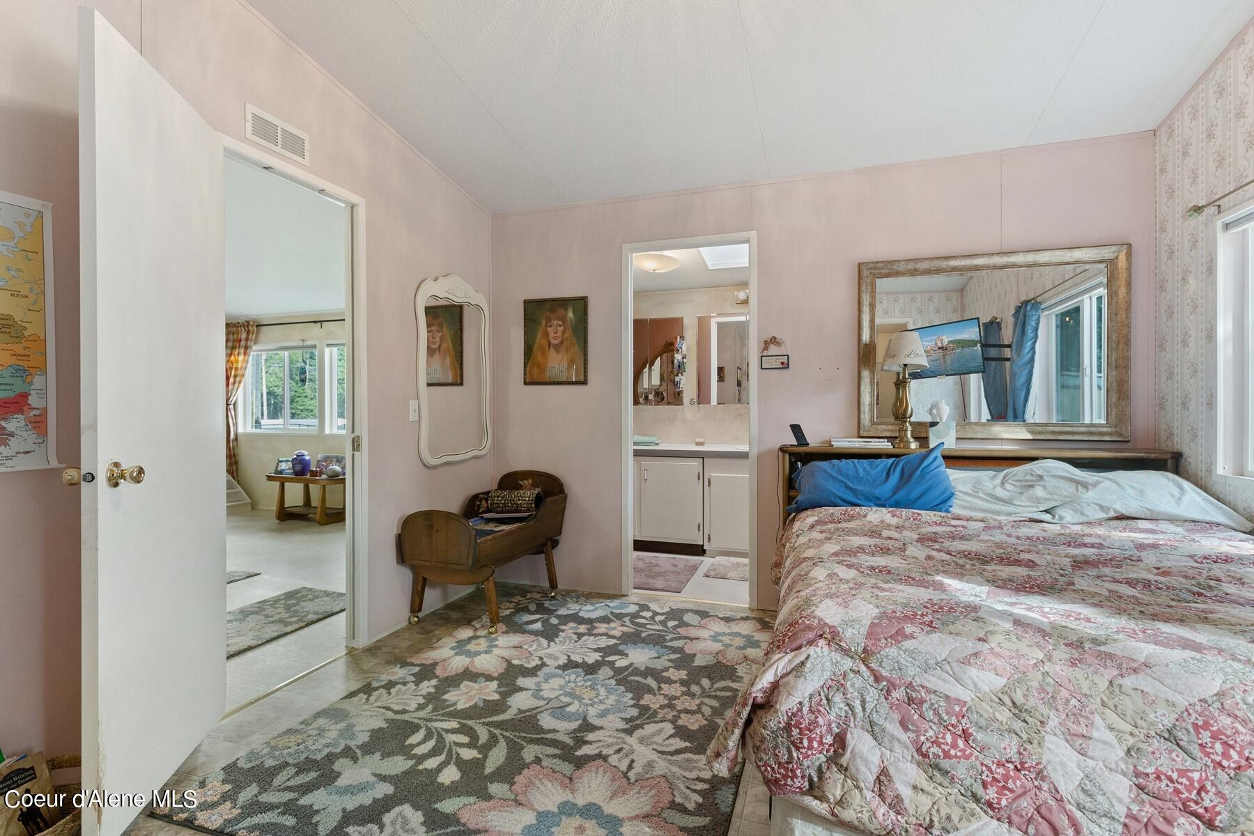 Furnished bedroom with pink walls, floral bedding, a large patterned rug, and an adjoining bathroom.