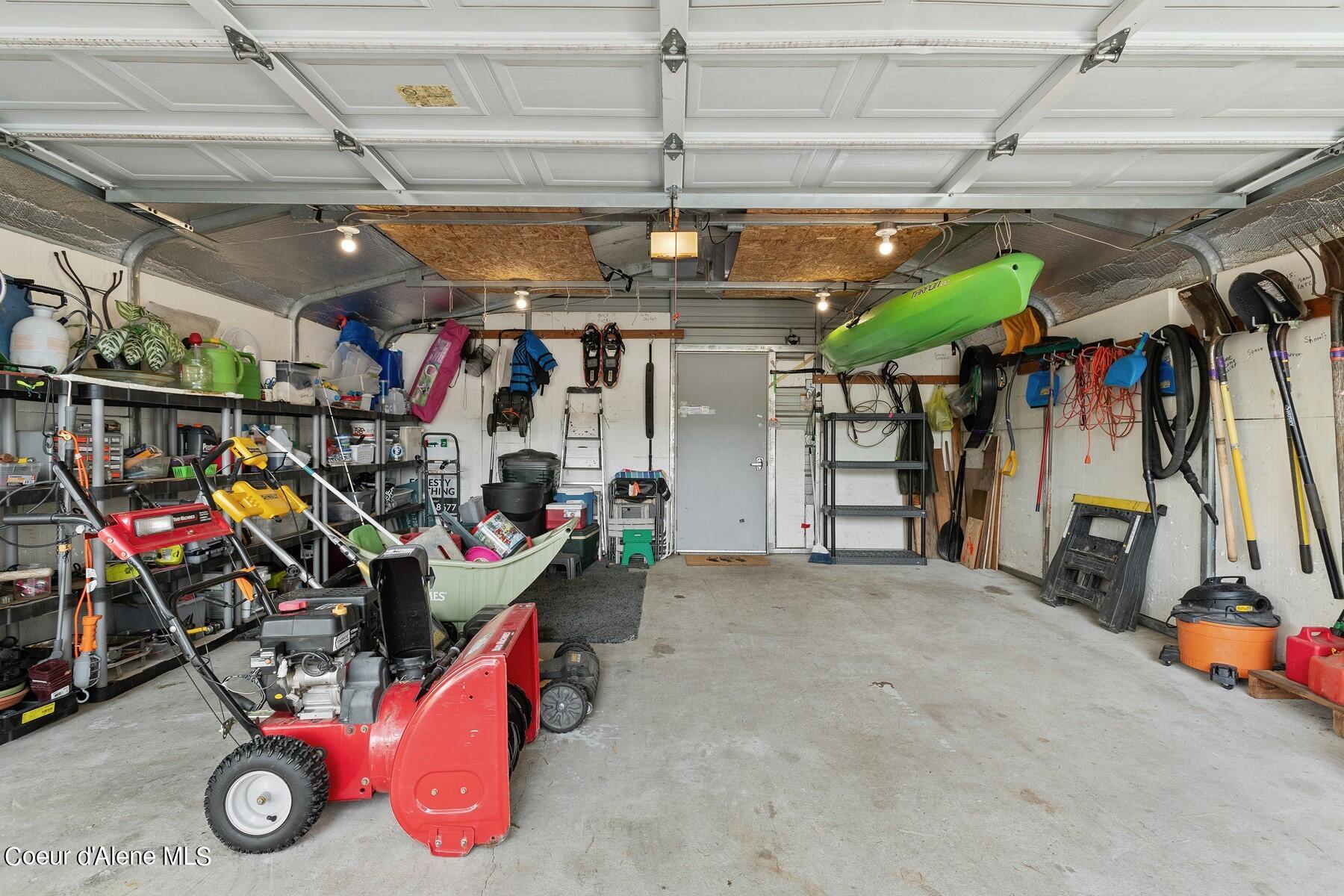 Garage filled with tools and lawn equipment, including a red snowblower and green kayak.
