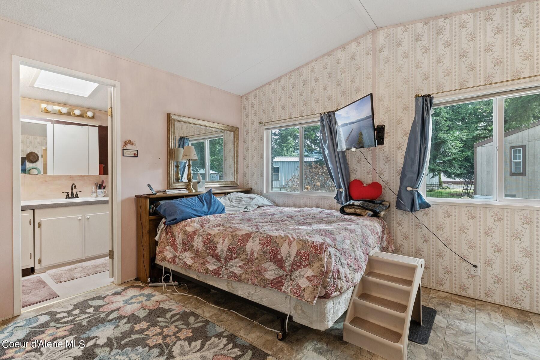 Bedroom with a floral patchwork quilt, patterned wallpaper, and large windows.