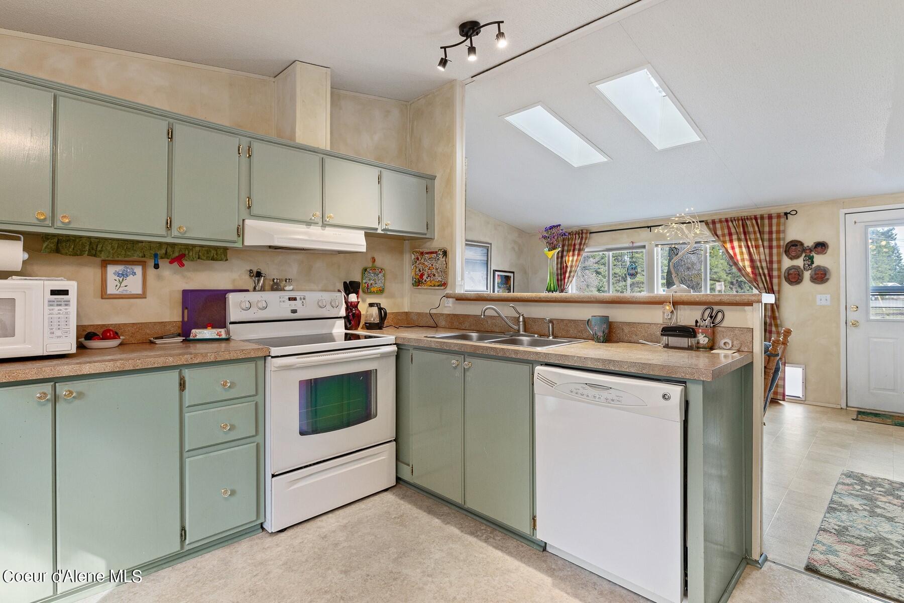 Kitchen with sage-green cabinets, white appliances, and a double sink beneath a window.