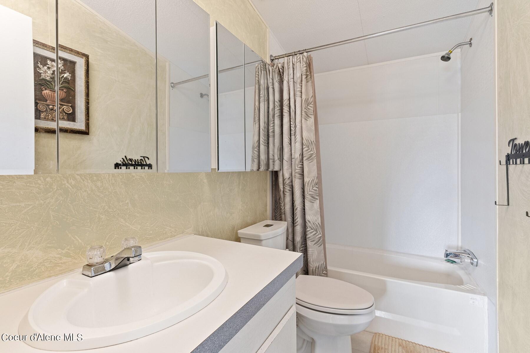 Bathroom with a white vanity, mirrored cabinets, and a bathtub behind a patterned shower curtain.