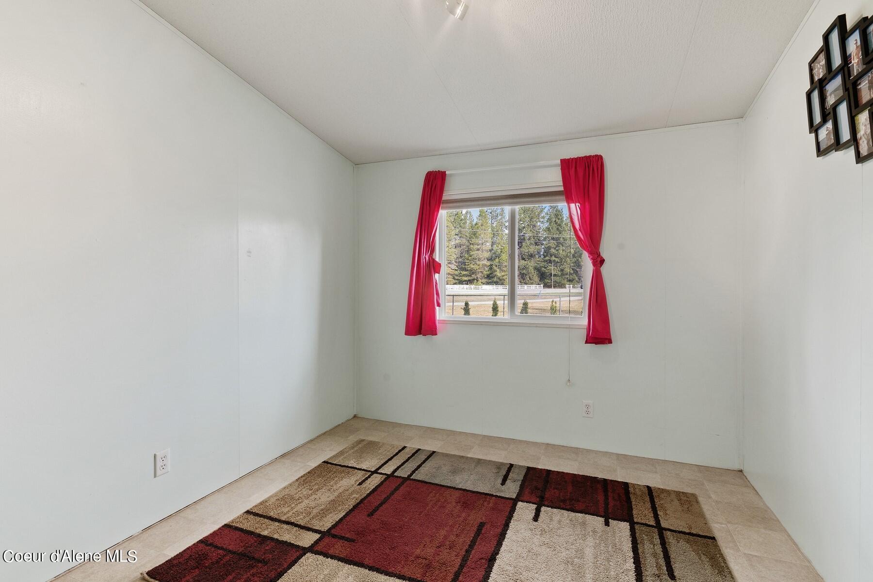 Mostly empty room with a geometric rug and a window framed by bright red curtains.