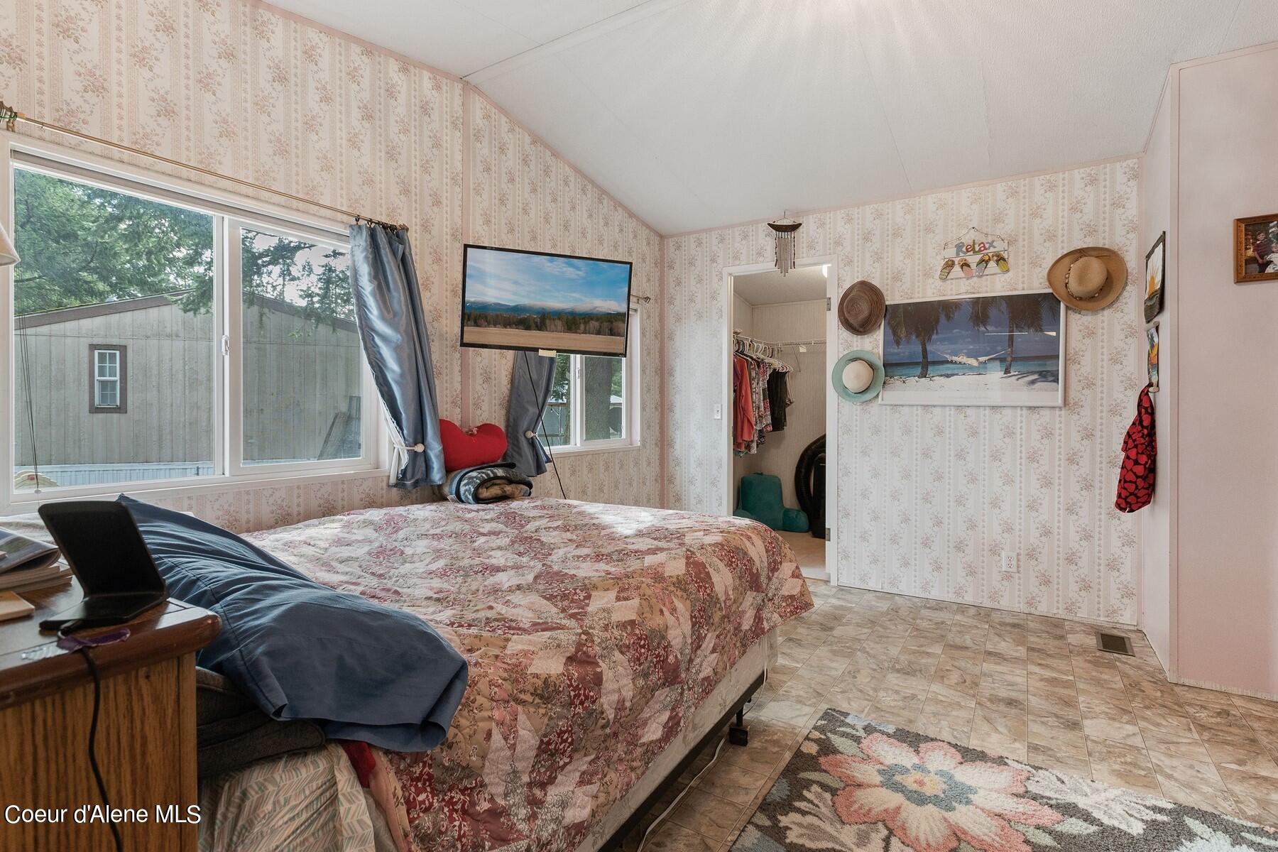 Bedroom with floral quilt, sloped ceiling, patterned wallpaper, and large windows.