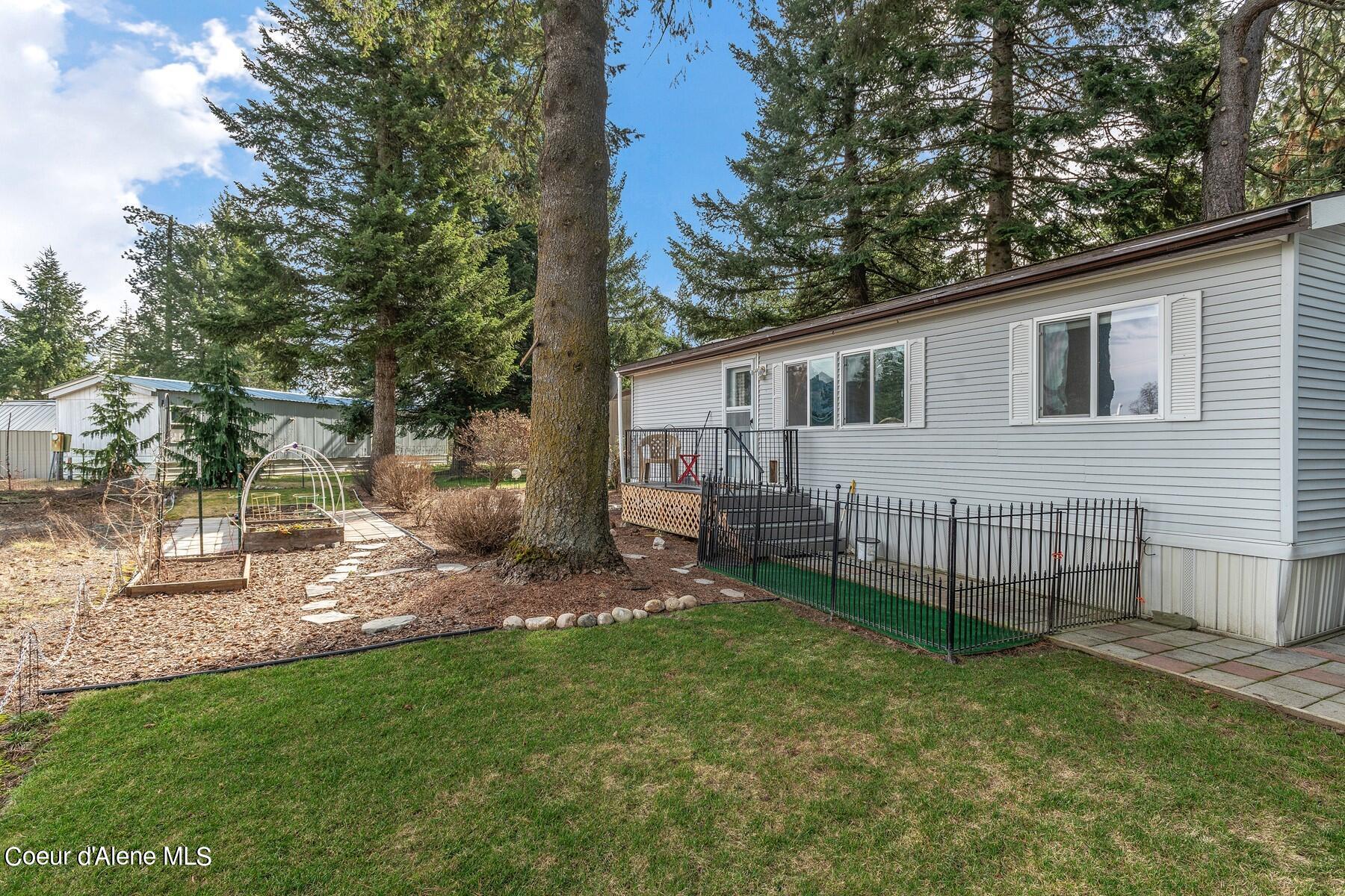 Light-gray home beside a fenced yard with mature evergreens, stepping stones, and a garden bed.