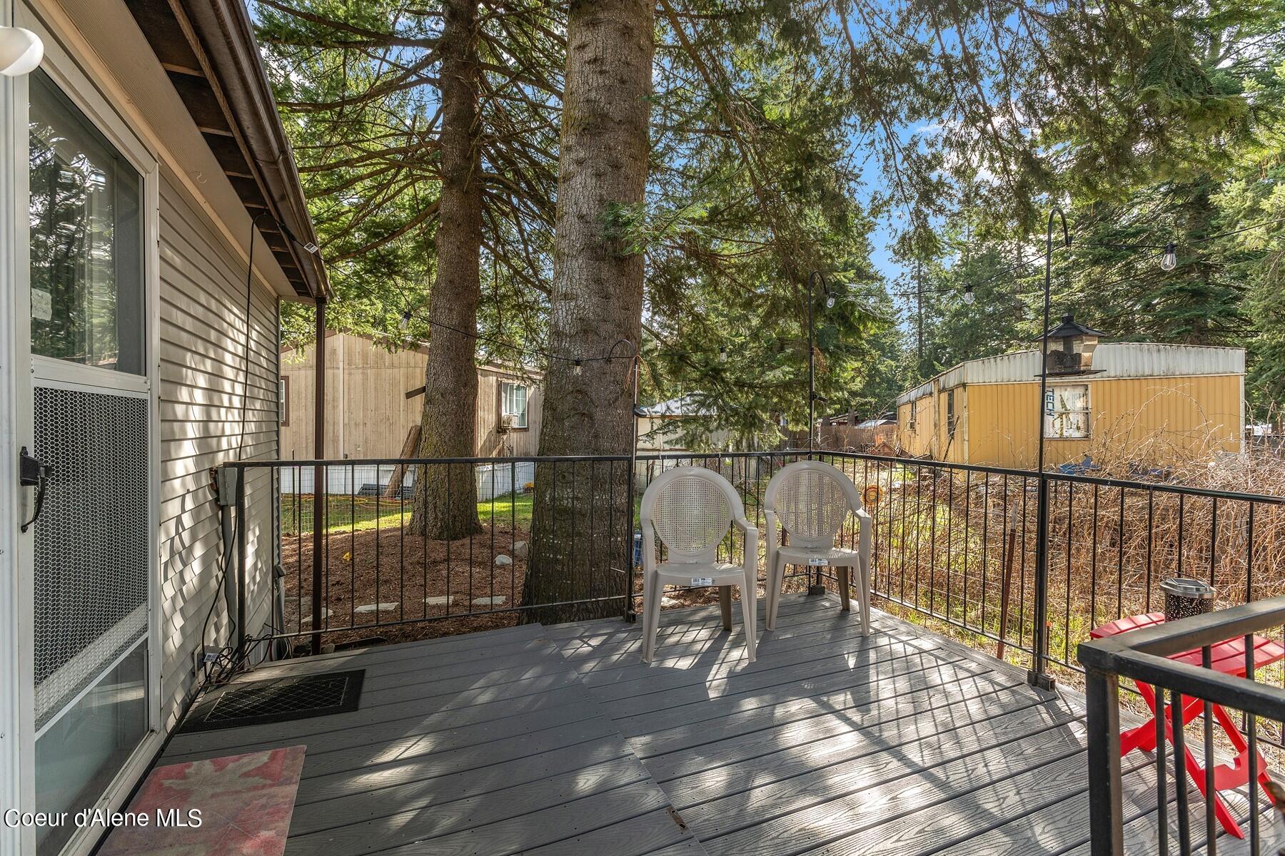 Gray deck with two white chairs and string lights beneath tall evergreen trees.