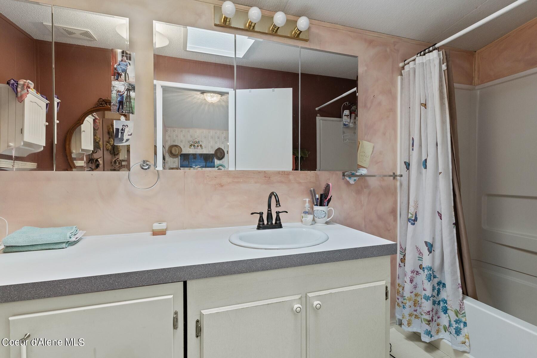 Bathroom with a wide mirrored vanity, oval sink, and floral shower curtain.