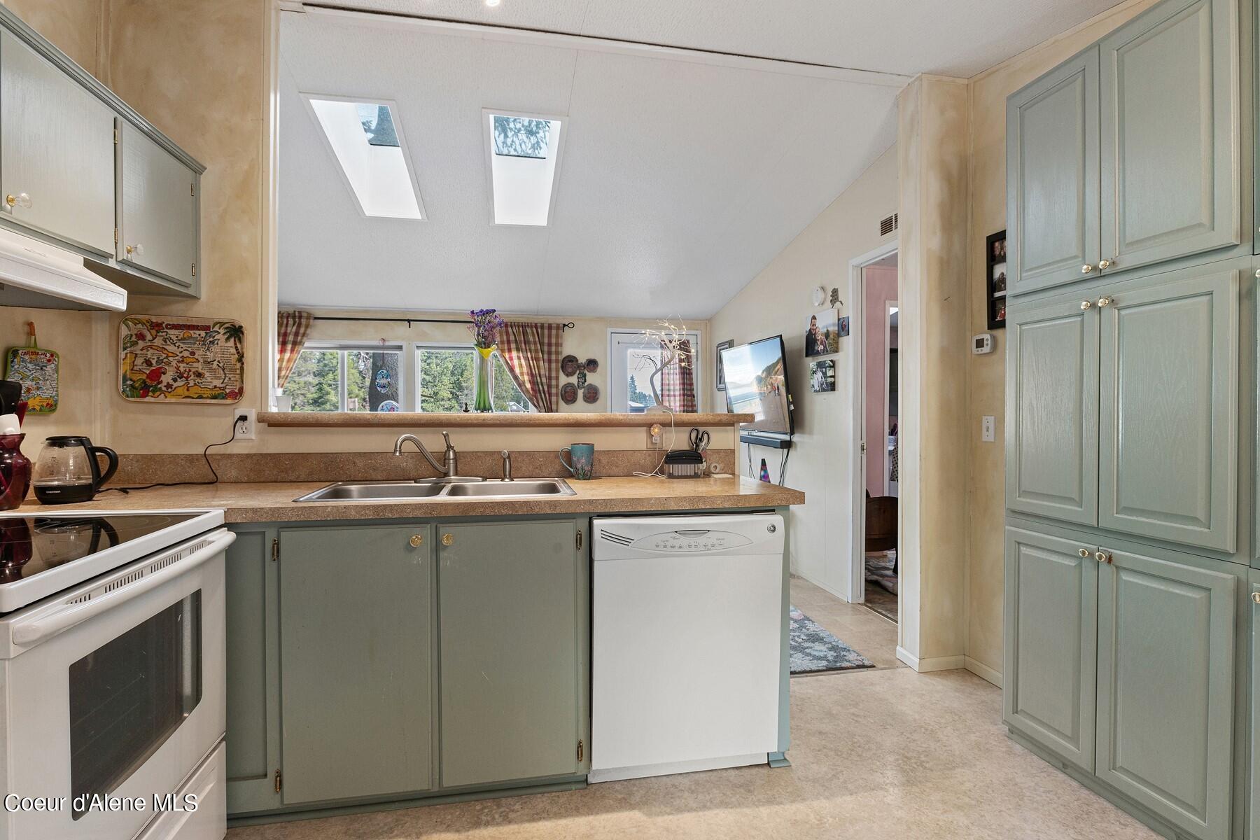 Kitchen with sage-green cabinets, a double-basin sink, white dishwasher, and two skylights.