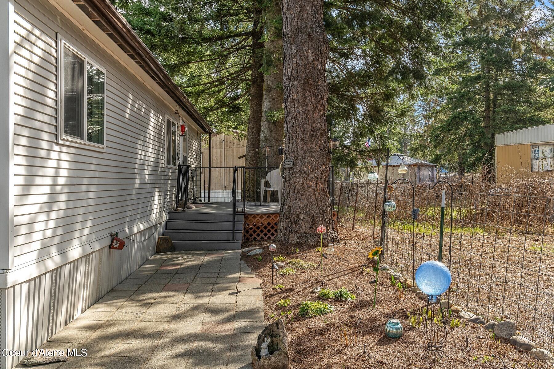 Home exterior with a paved walkway, raised deck, mature evergreens, and fenced garden.