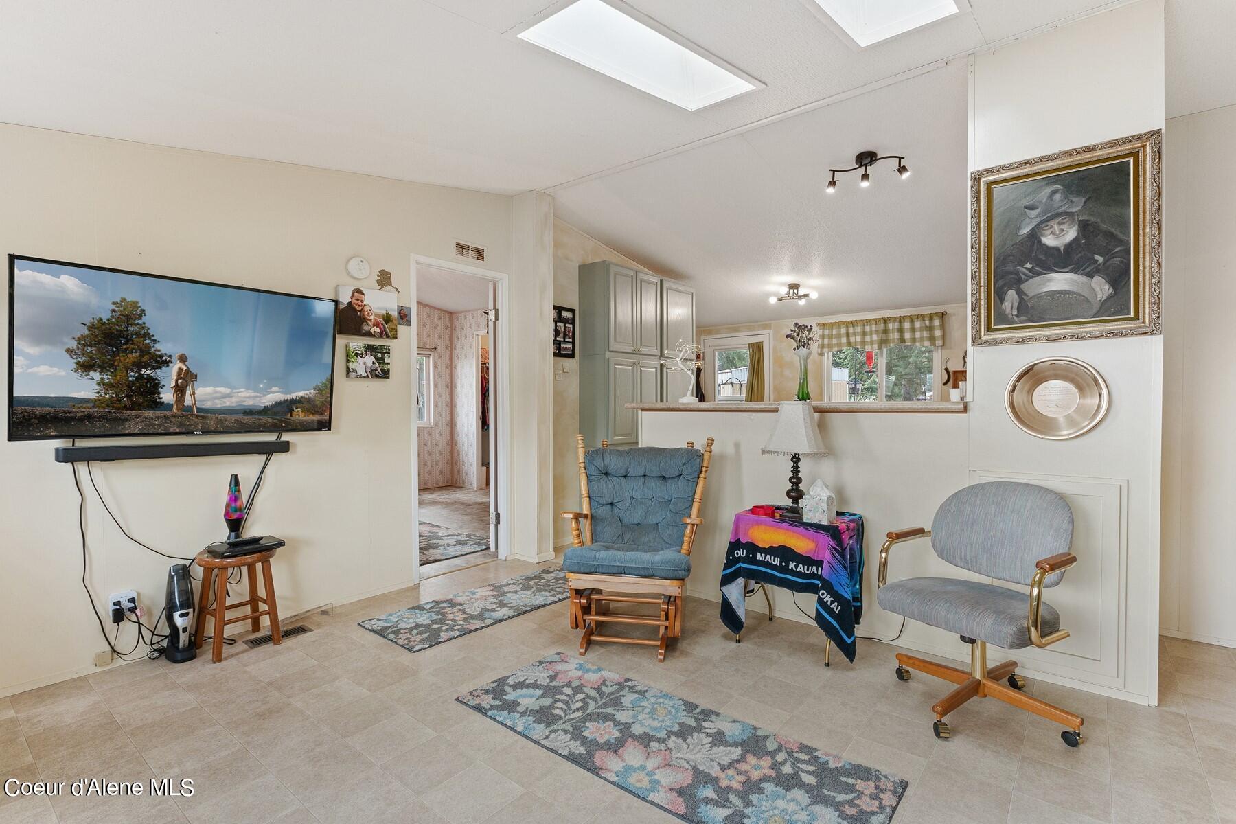 Furnished living room with a wall-mounted television, floral rugs, and an opening to the kitchen.